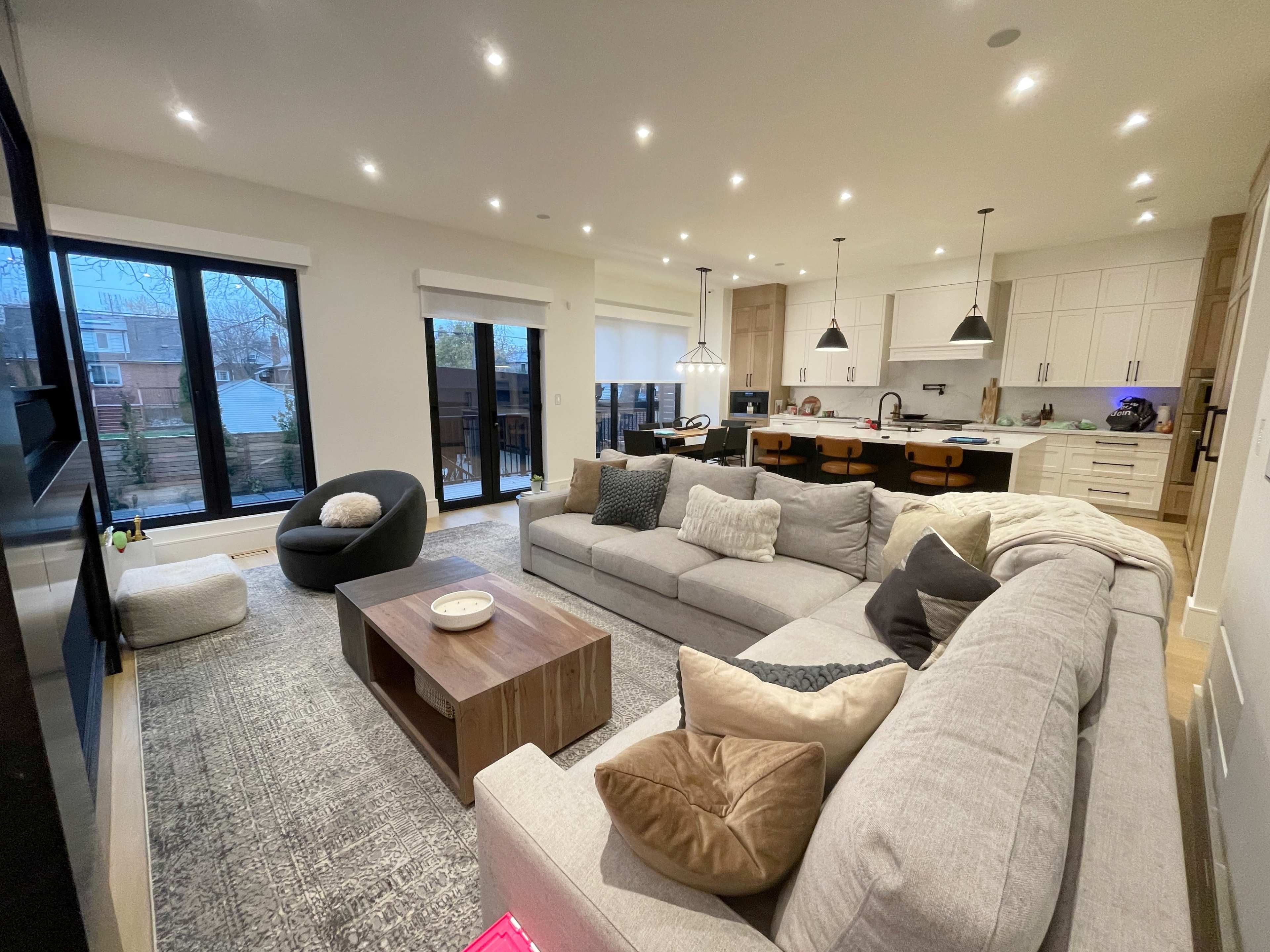 A modern, open-concept living area featuring a large sectional sofa, a coffee table, and a view of a well-lit kitchen with island seating.