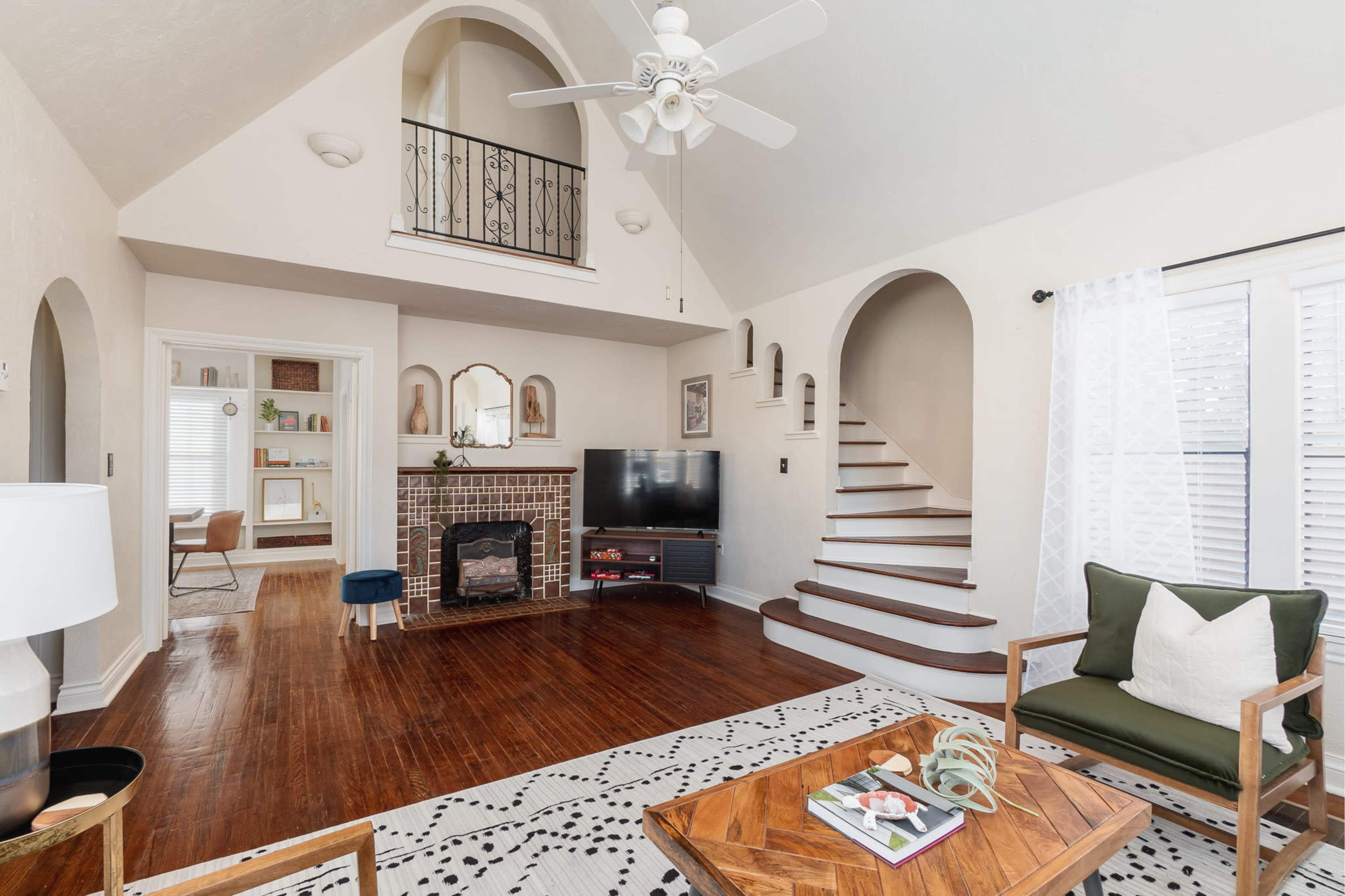 A living room with a fireplace, a TV, and a staircase leading to an upper level beneath a vaulted ceiling.
