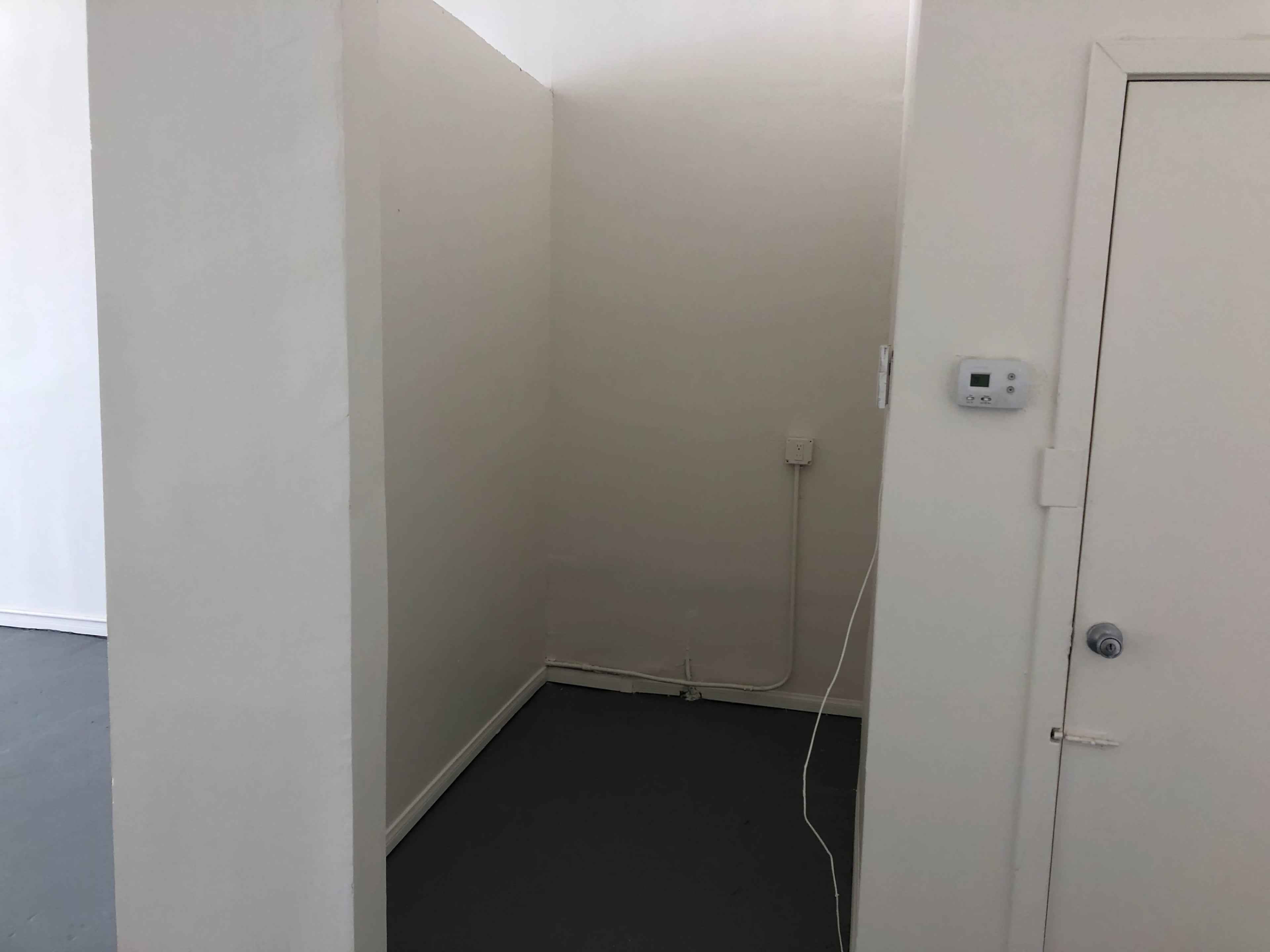 The image shows a small, empty corner of a room with white walls and a door at one end.