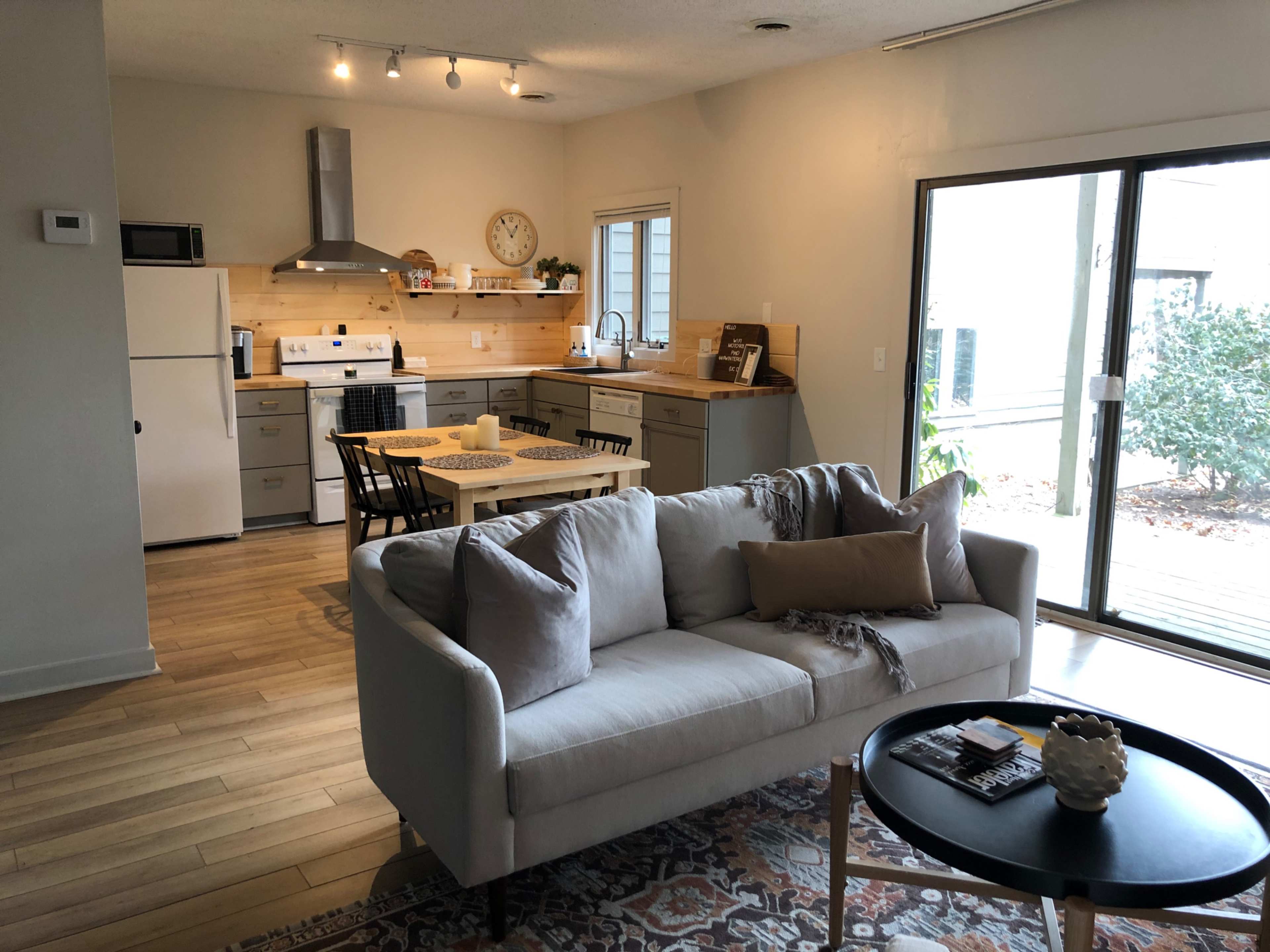 A modern kitchen and living area with a sofa, dining table, and sliding glass doors leading to an outdoor space.