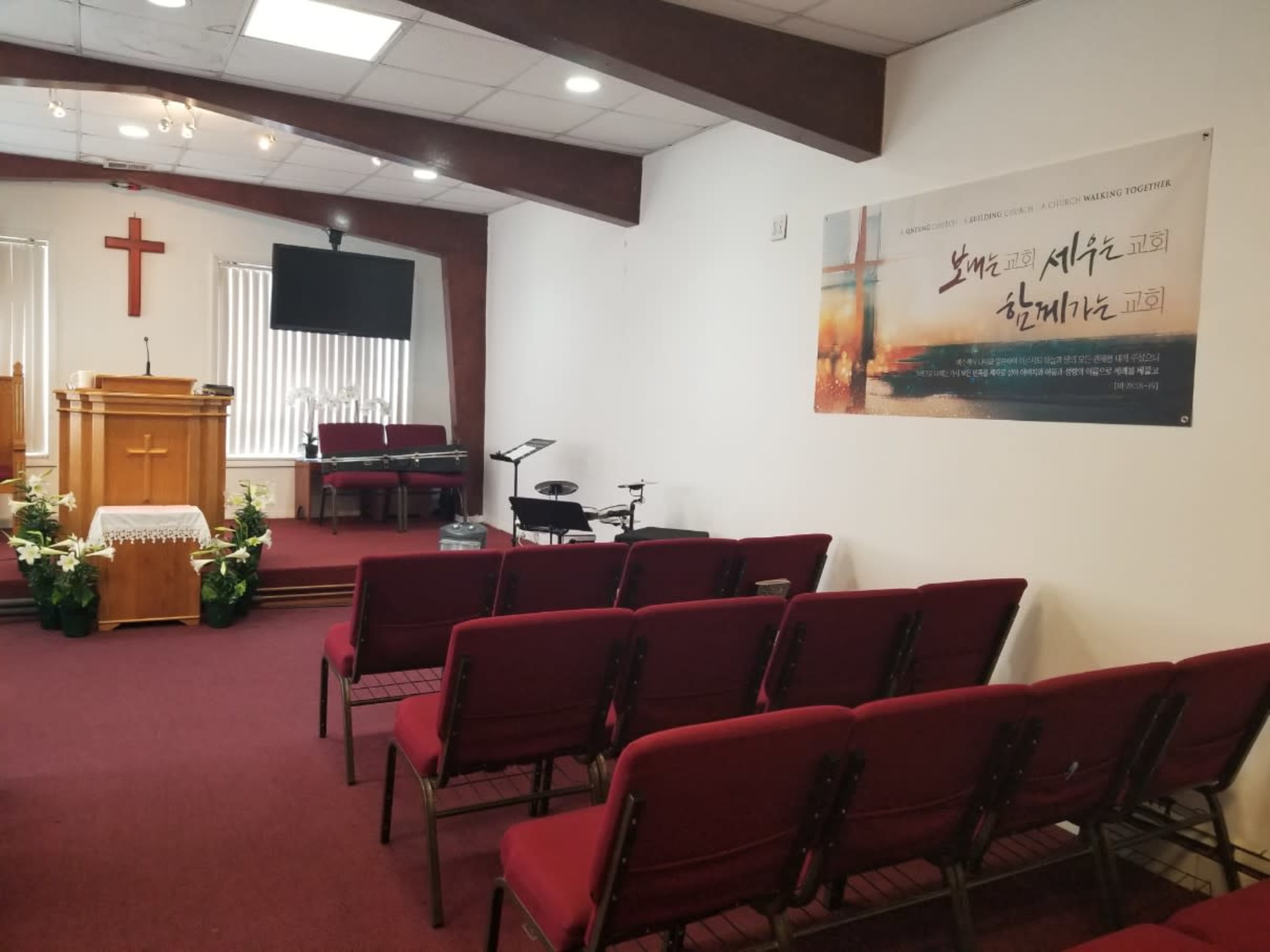 The image shows the interior of a church with a wooden pulpit, rows of red chairs, and a banner on the wall displaying text in an Asian script.