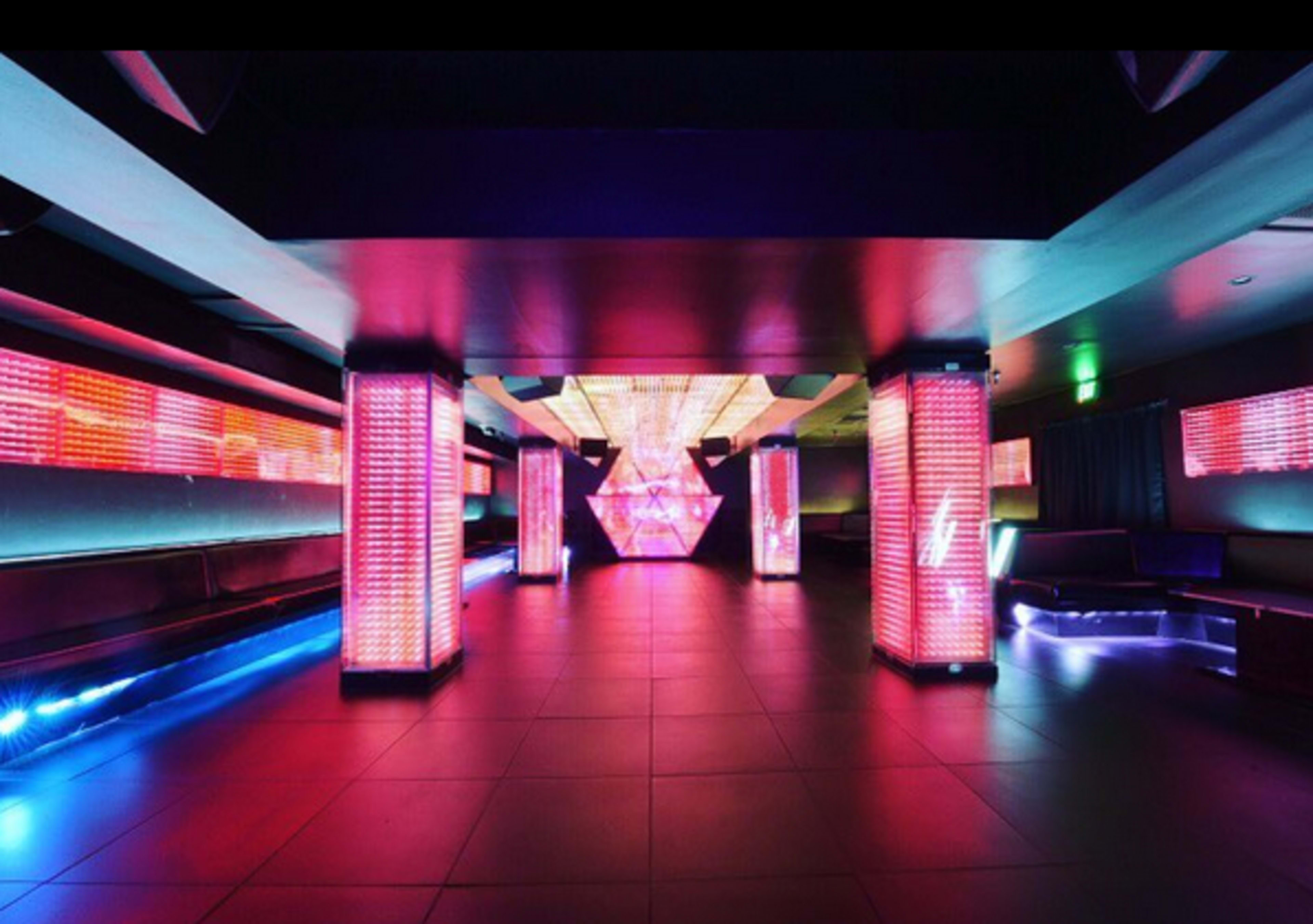 A modern nightclub interior with bright, colorful LED lighting and a geometric light installation at the center.