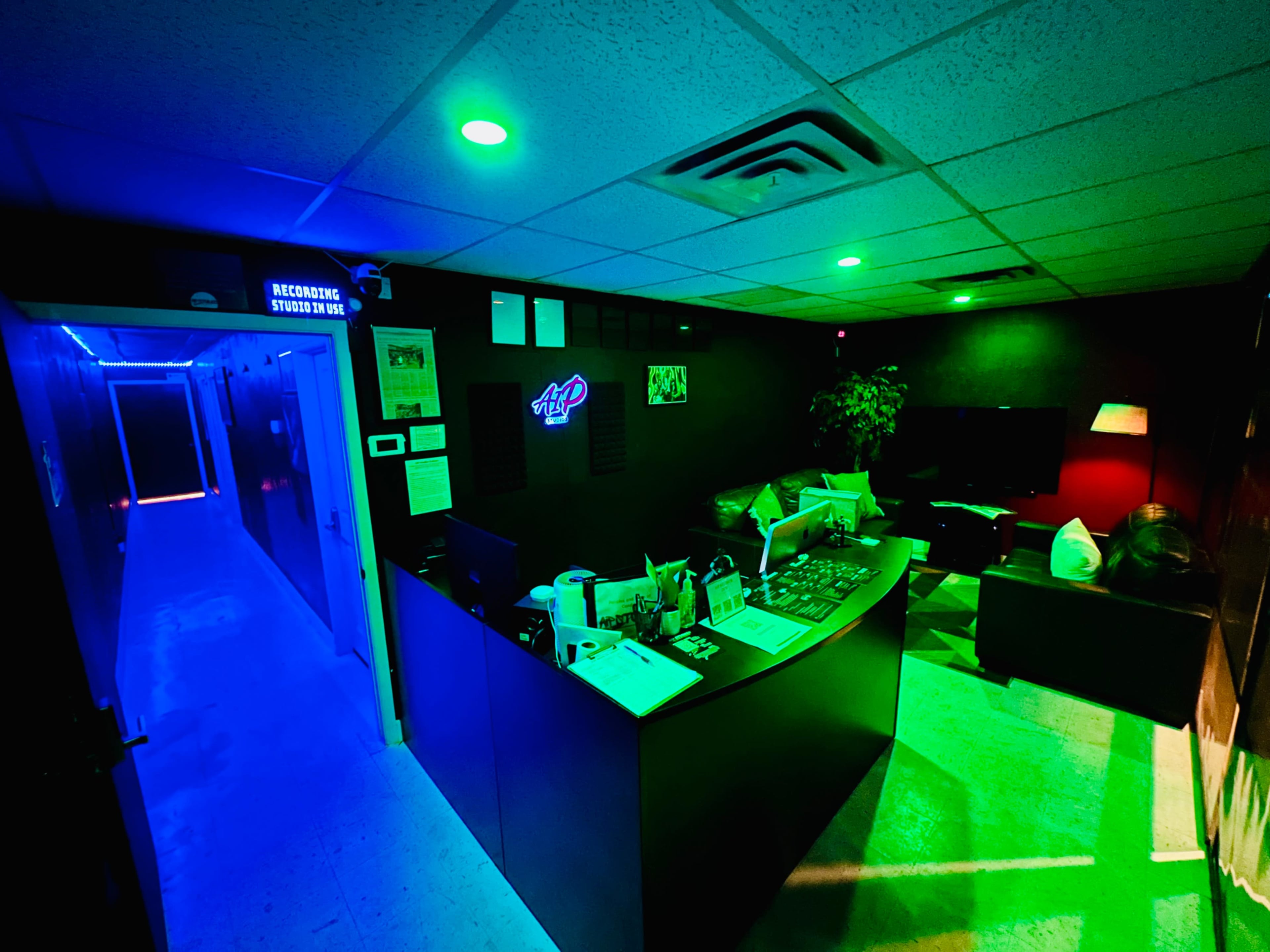 A dimly lit office space featuring a reception area with a desk, green lights, and a hallway in the background.