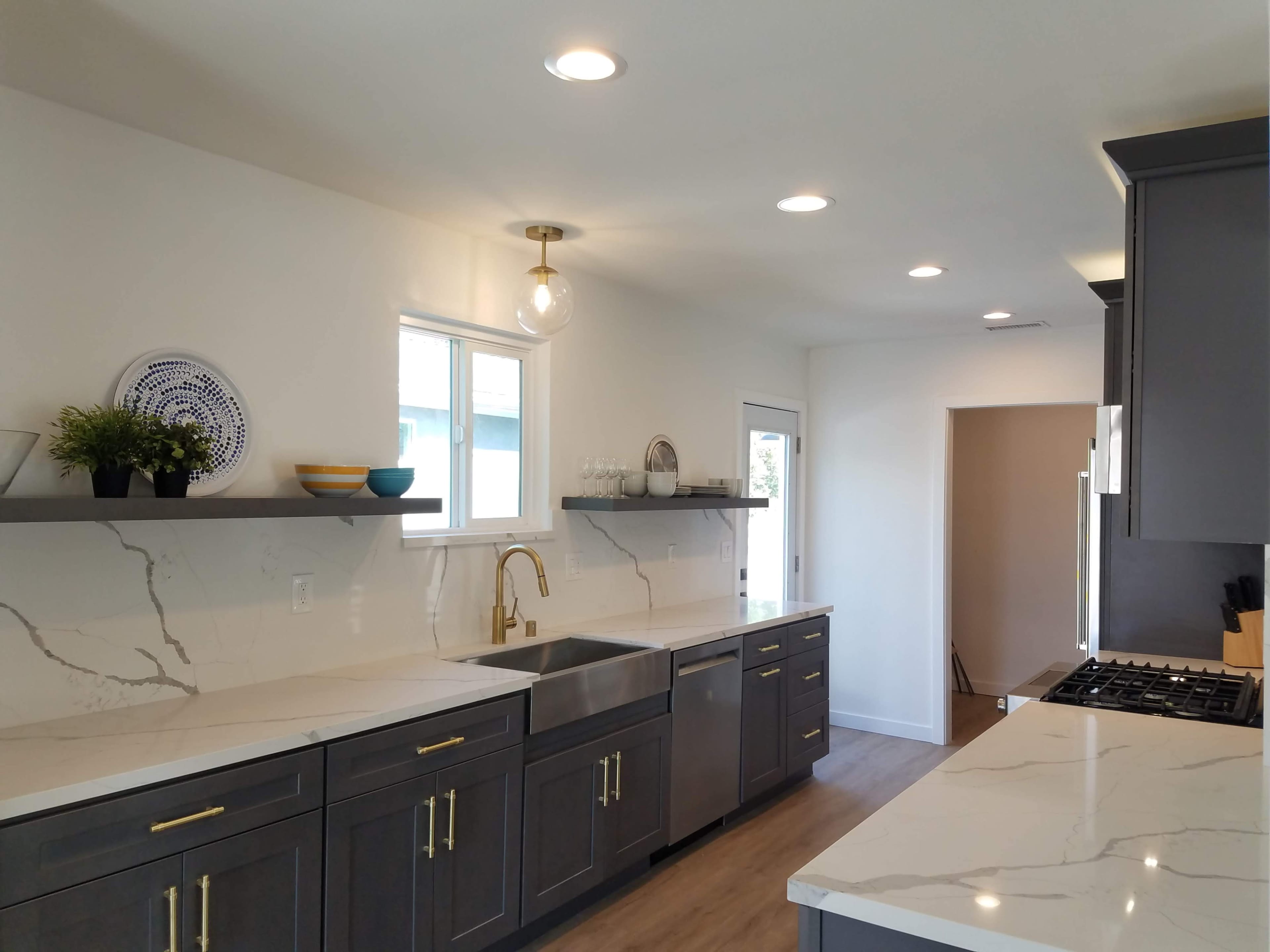 A modern kitchen features grey cabinetry, white marble countertops, and open shelving with decorative items.