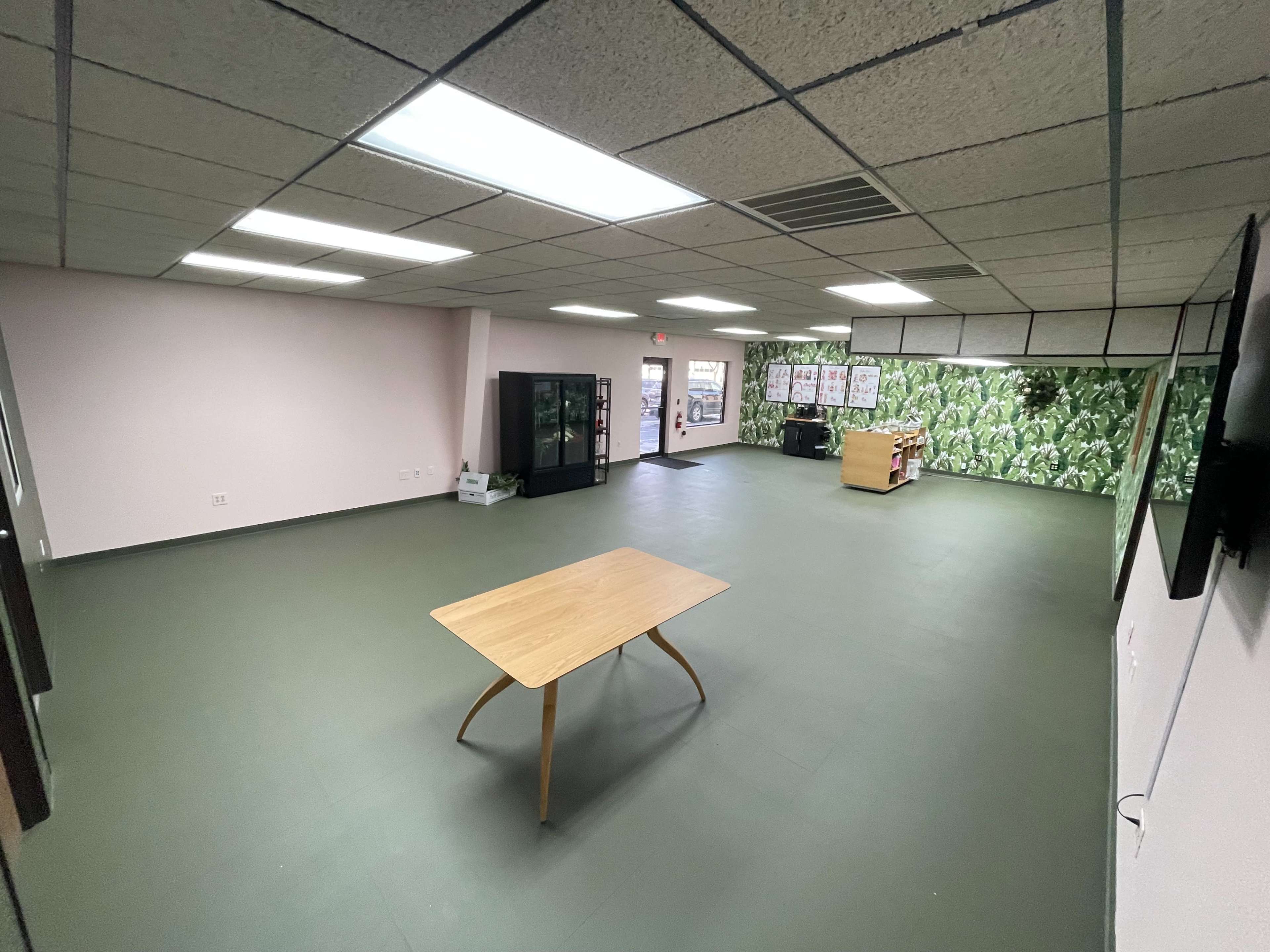 A spacious, empty room with a wooden table in the center, surrounding walls painted in light colors, and one wall featuring a green patterned mural.
