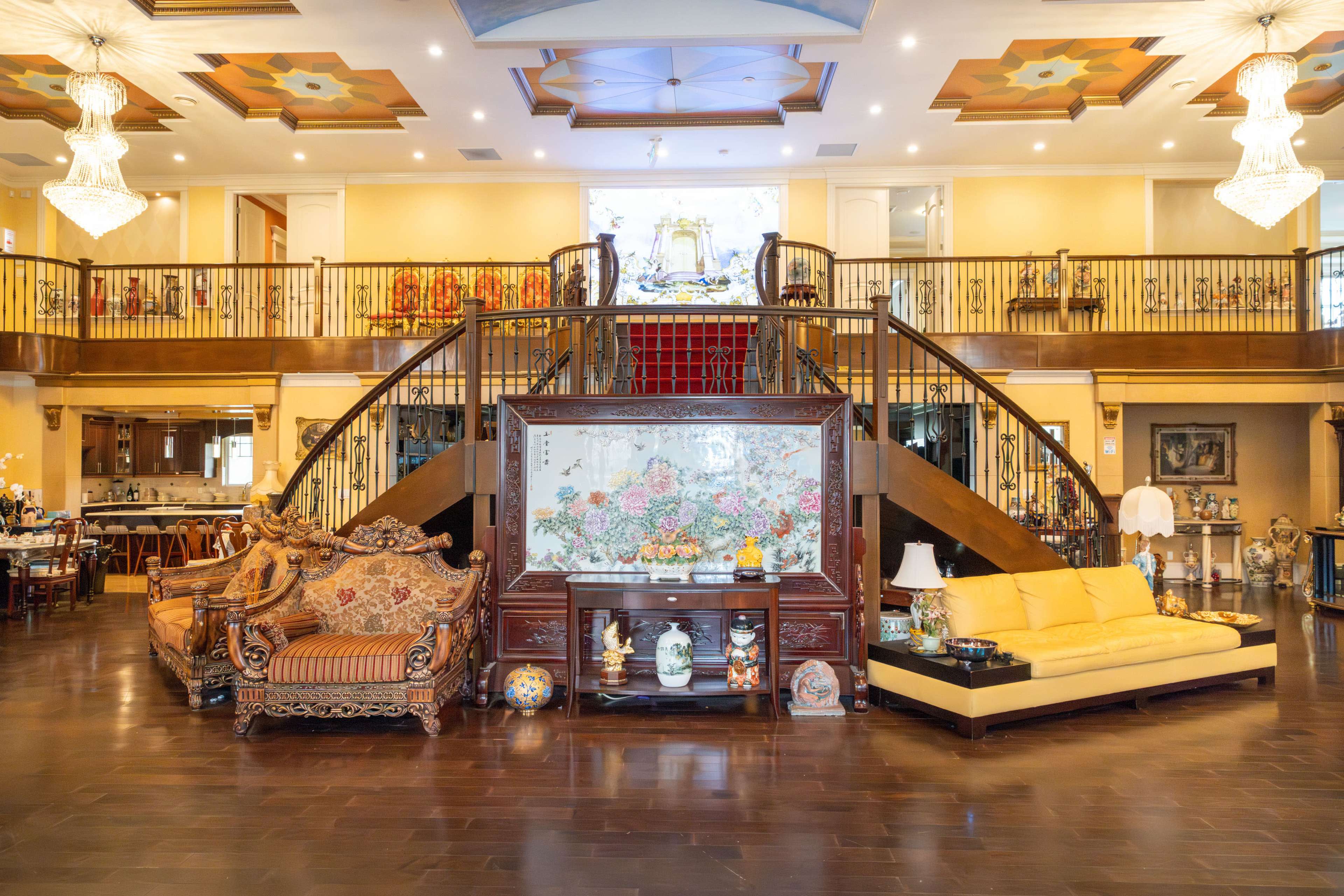 The image features an elaborate interior of a spacious living room with a grand staircase, elegant furniture, and decorative art pieces.