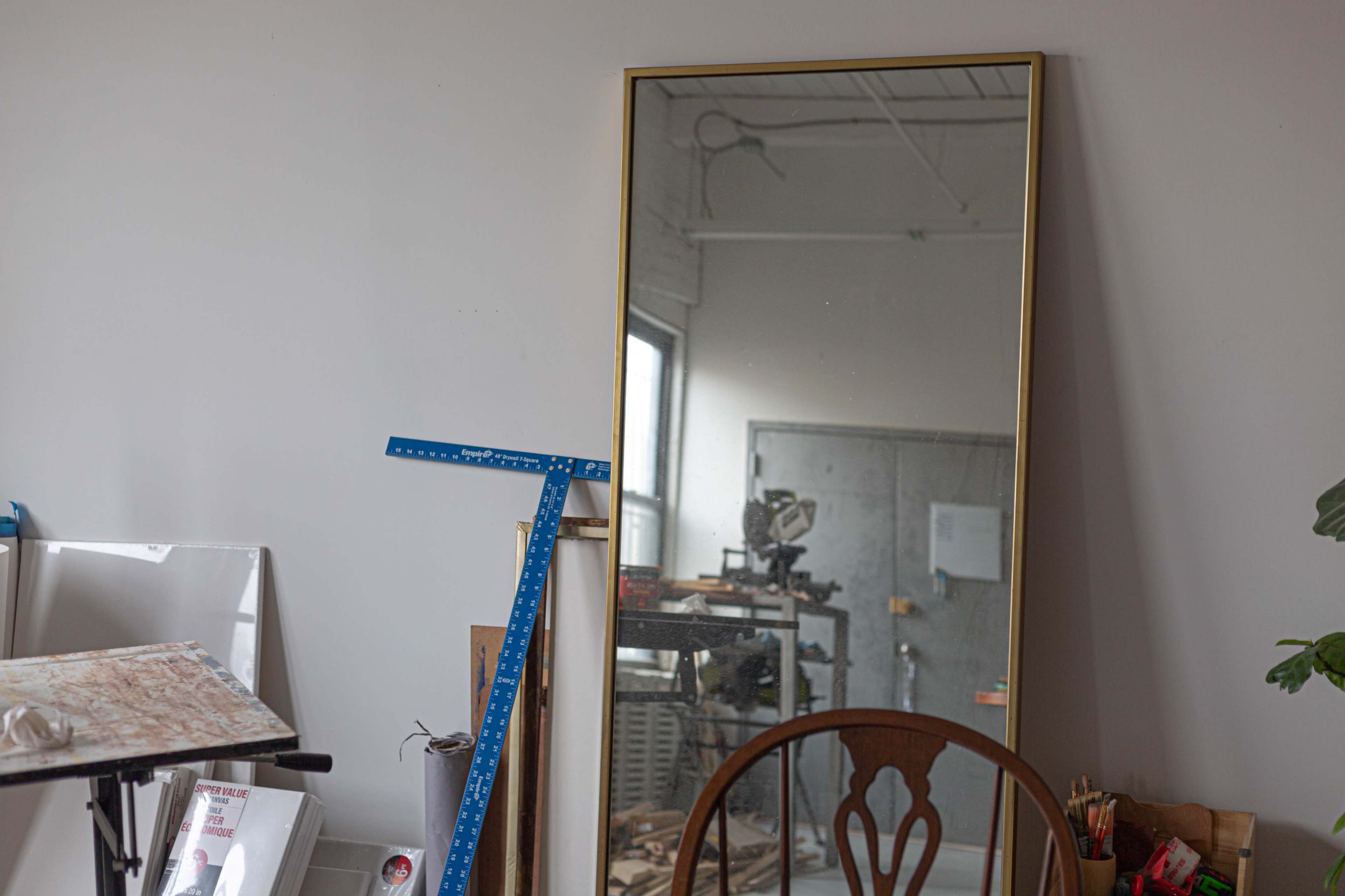 A large framed mirror stands against a wall near a workshop, reflecting the interior space and tools.