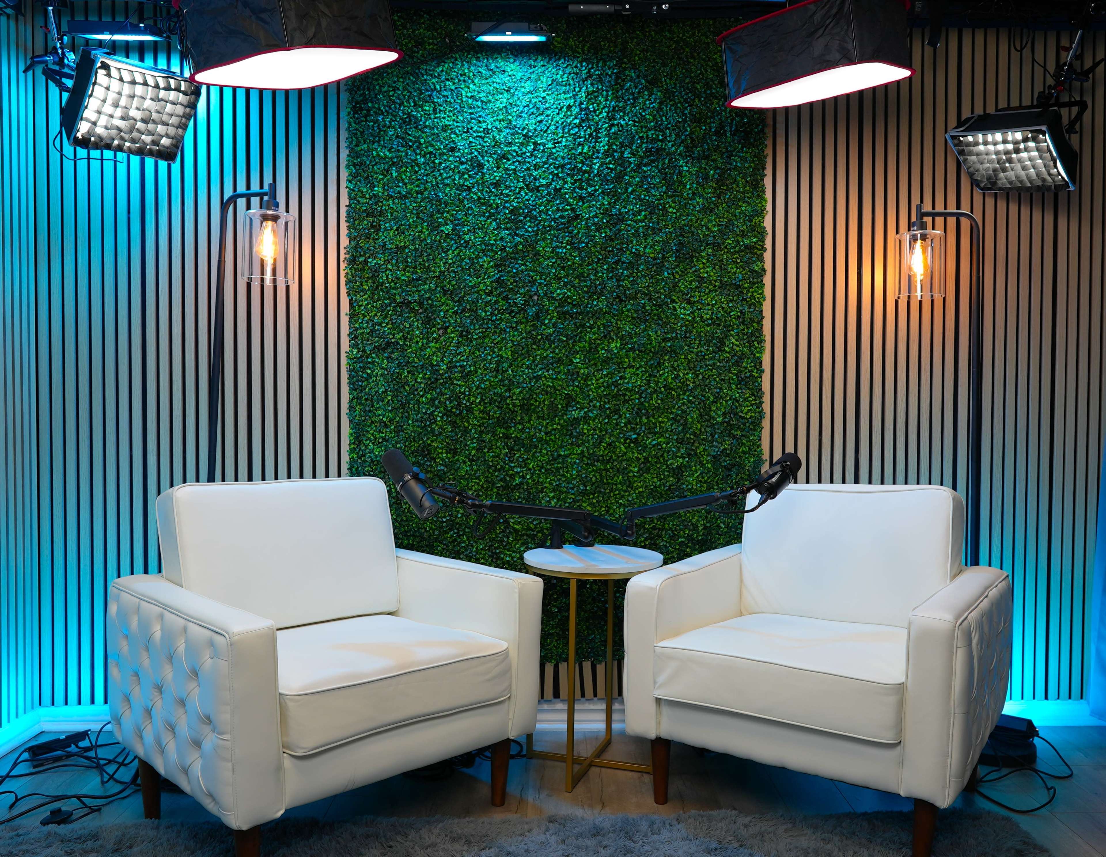 The image features two white upholstered chairs positioned facing each other in a studio setting with a green wall and various lighting fixtures.