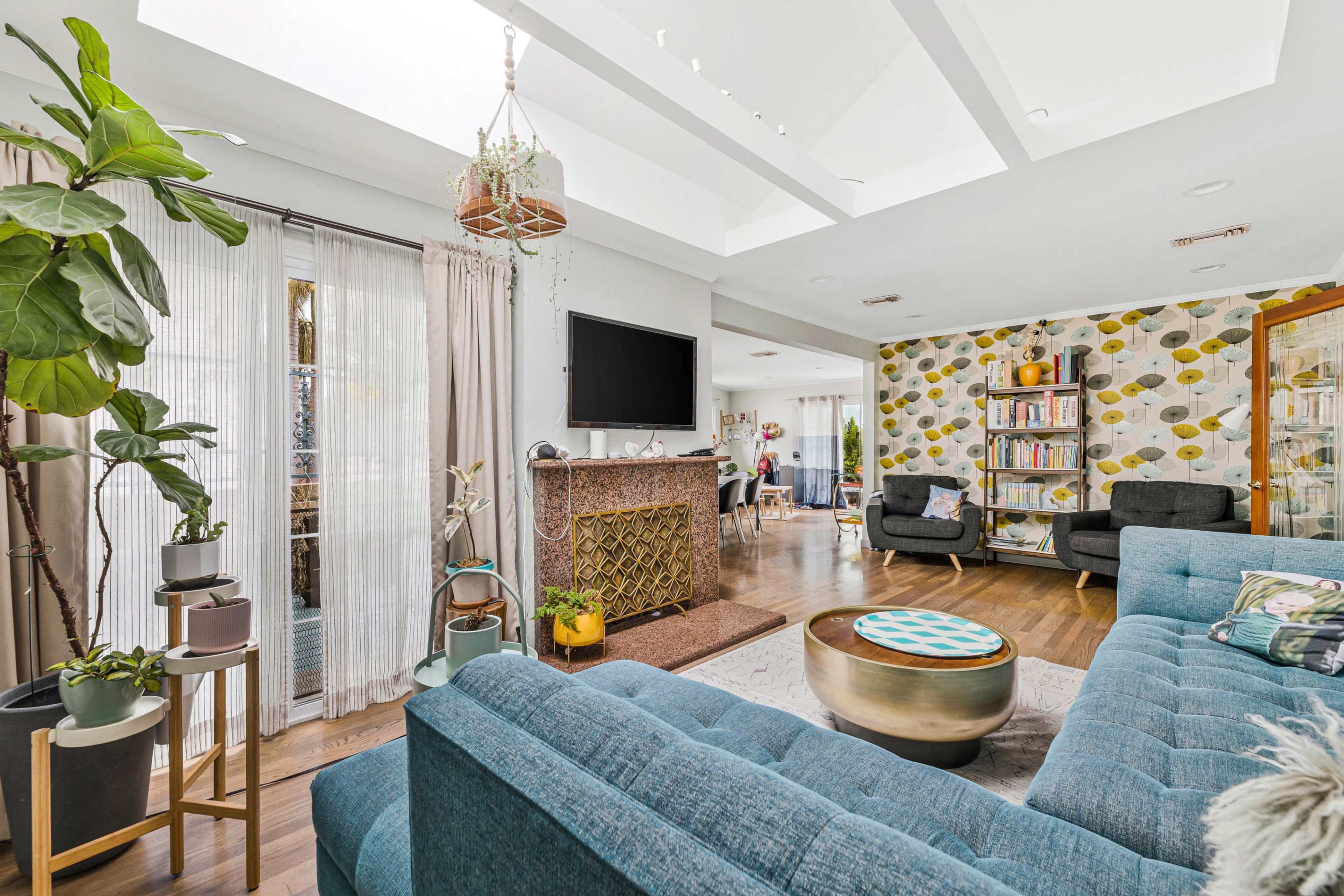 A bright living room features a blue sectional sofa, a decorative fireplace, and a wall covered in geometric patterned wallpaper.