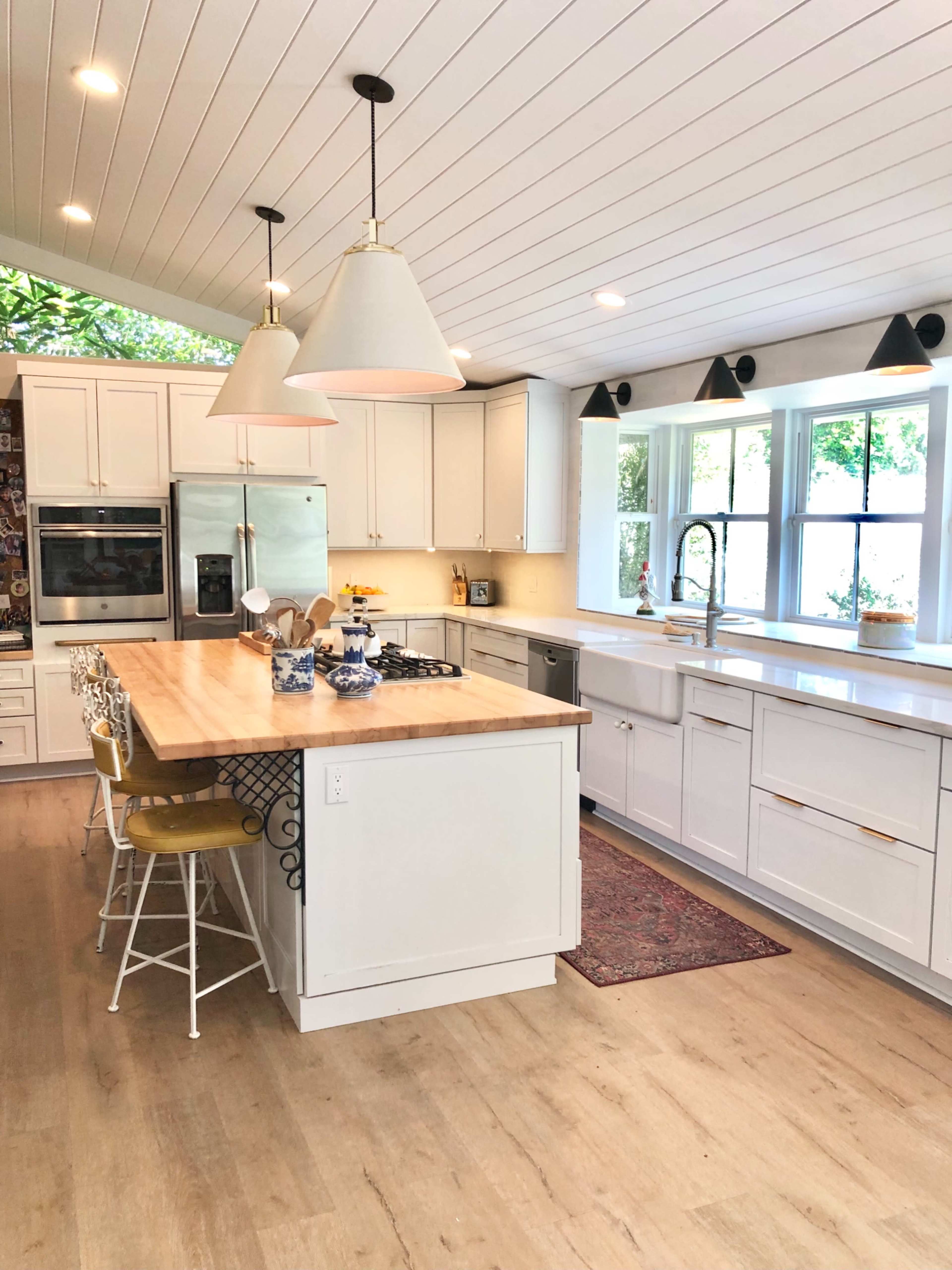 A modern kitchen with white cabinetry, a central wooden island, and large windows allowing natural light to fill the space.