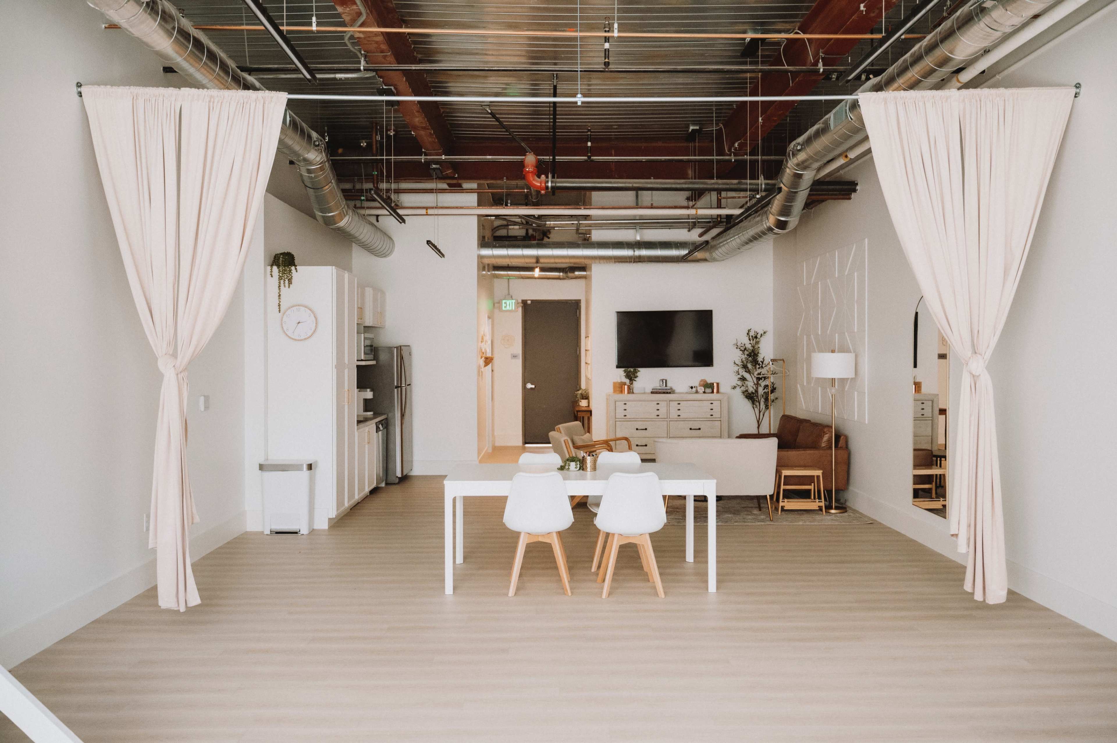 A spacious, modern interior with a dining table and chairs in the foreground, light-colored flooring, and a kitchen area in the background.