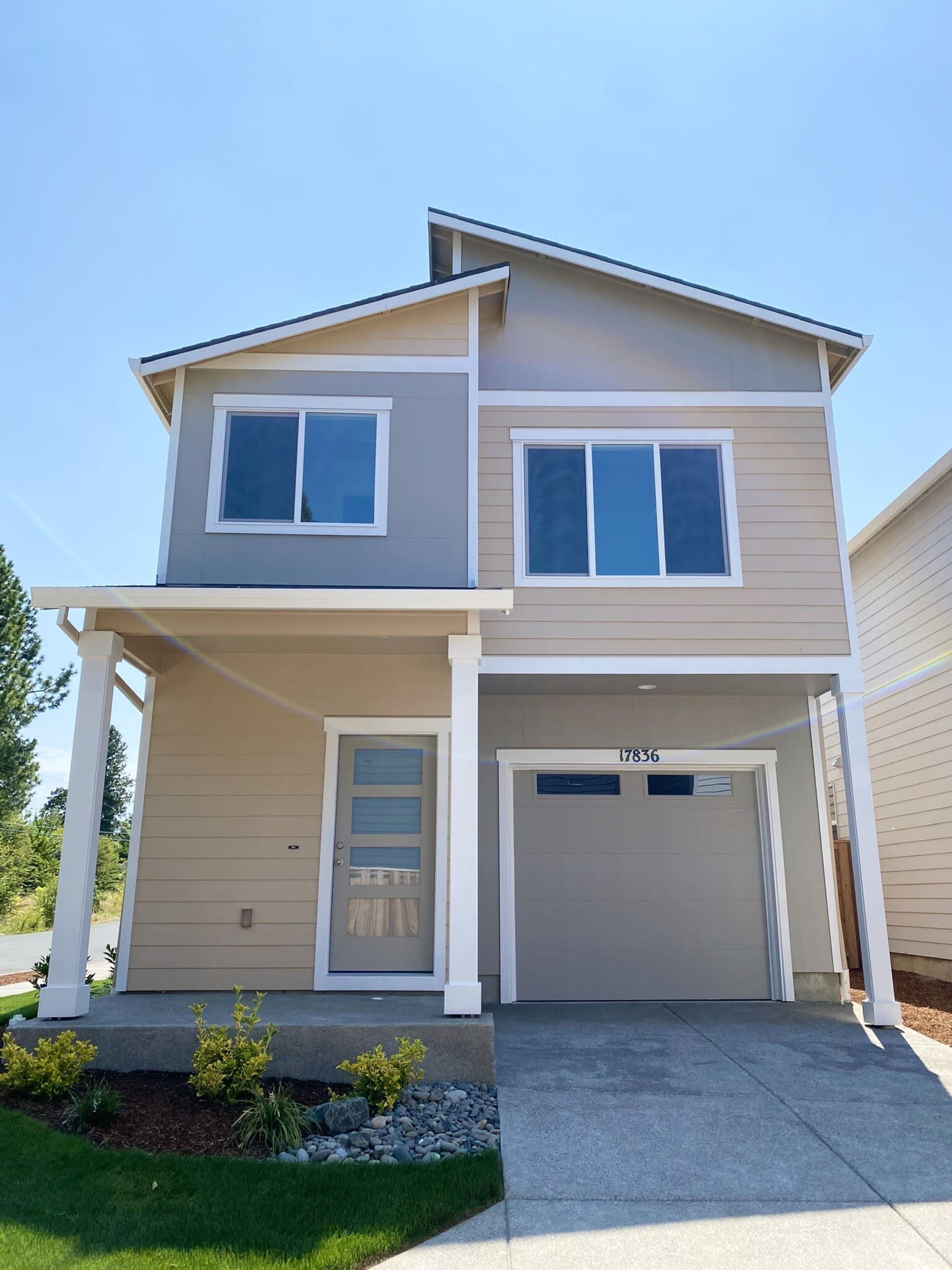 The image shows a two-story modern house with a light-colored exterior and a concrete driveway.