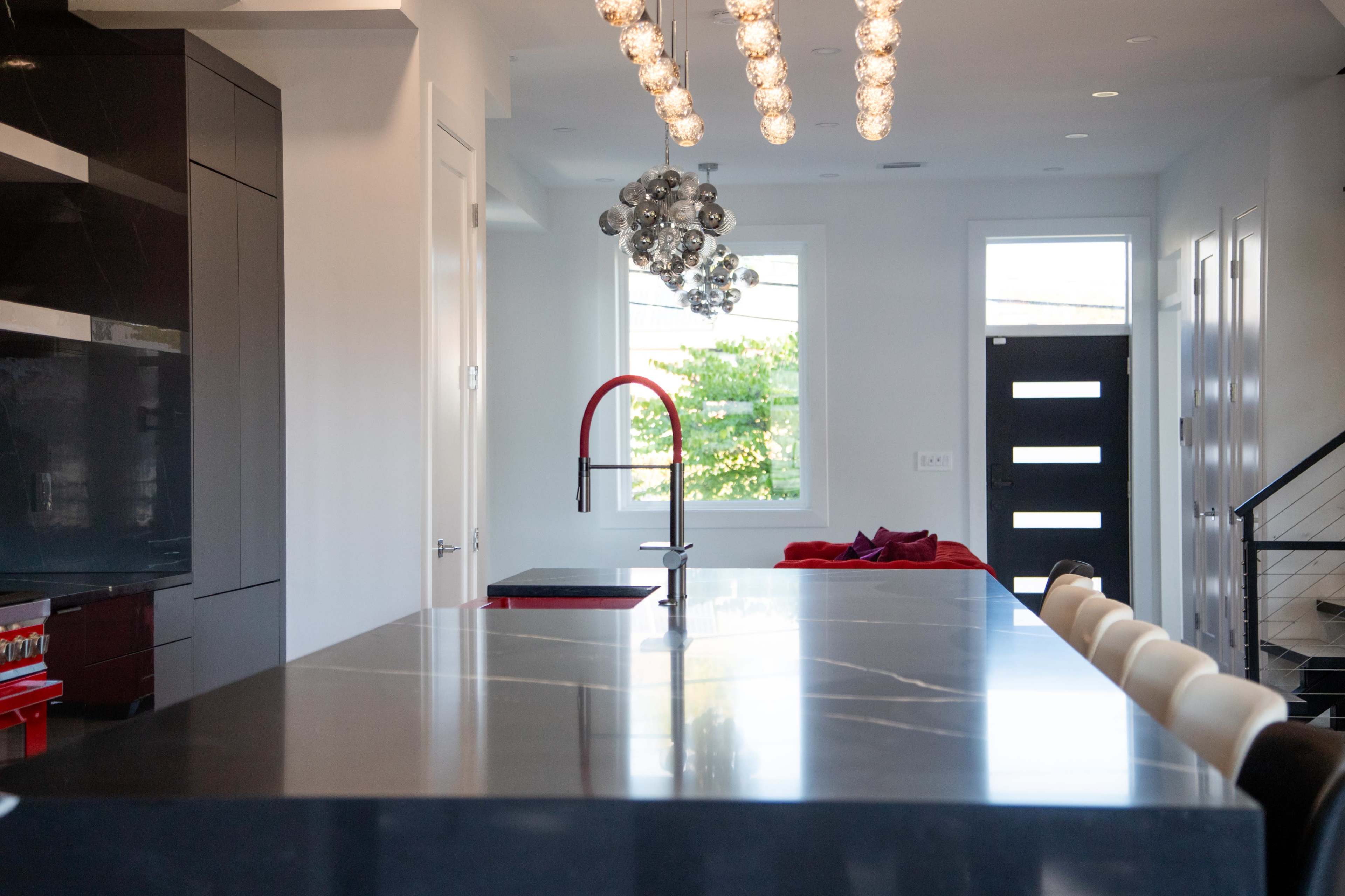 The image shows a modern kitchen with a large black countertop, sleek cabinetry, and a decorative chandelier above the island.