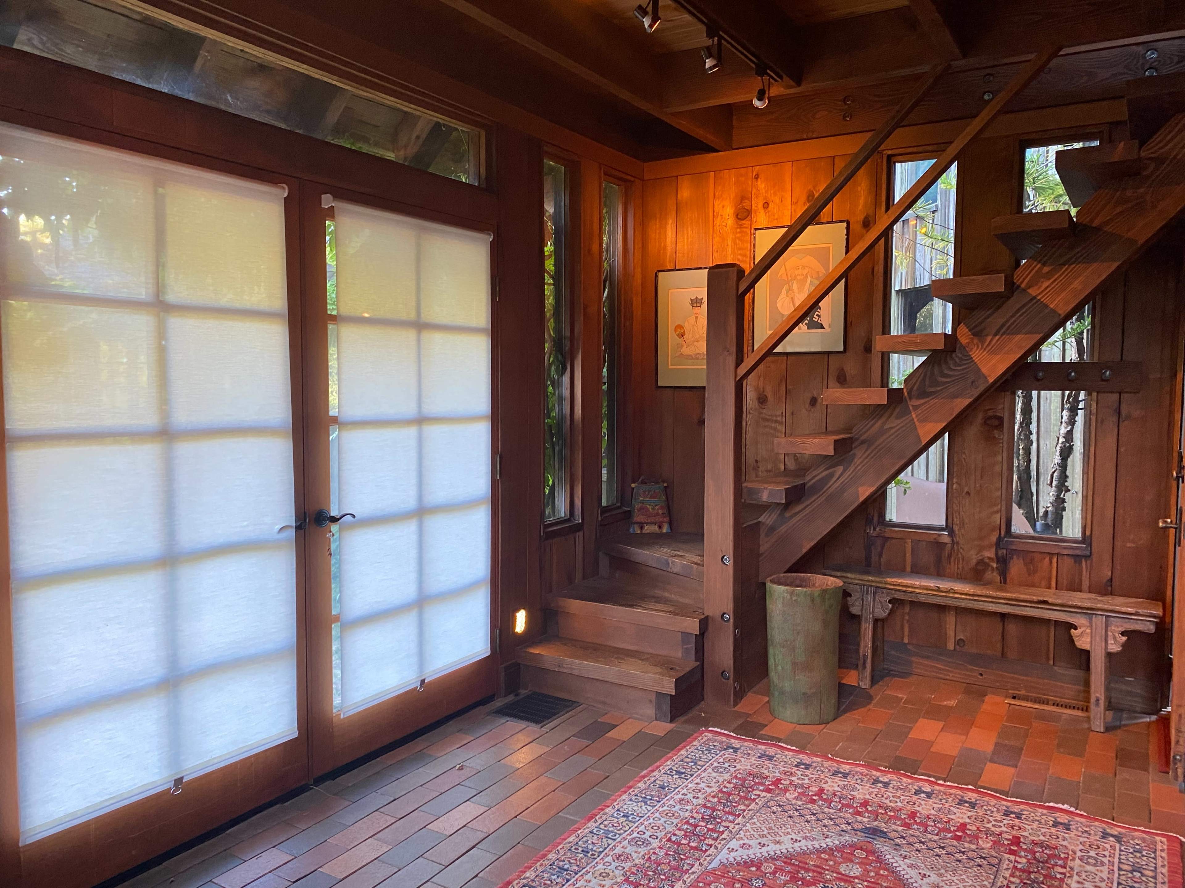 A wooden interior space featuring a staircase, a pair of glass doors, and a patterned rug on the floor.