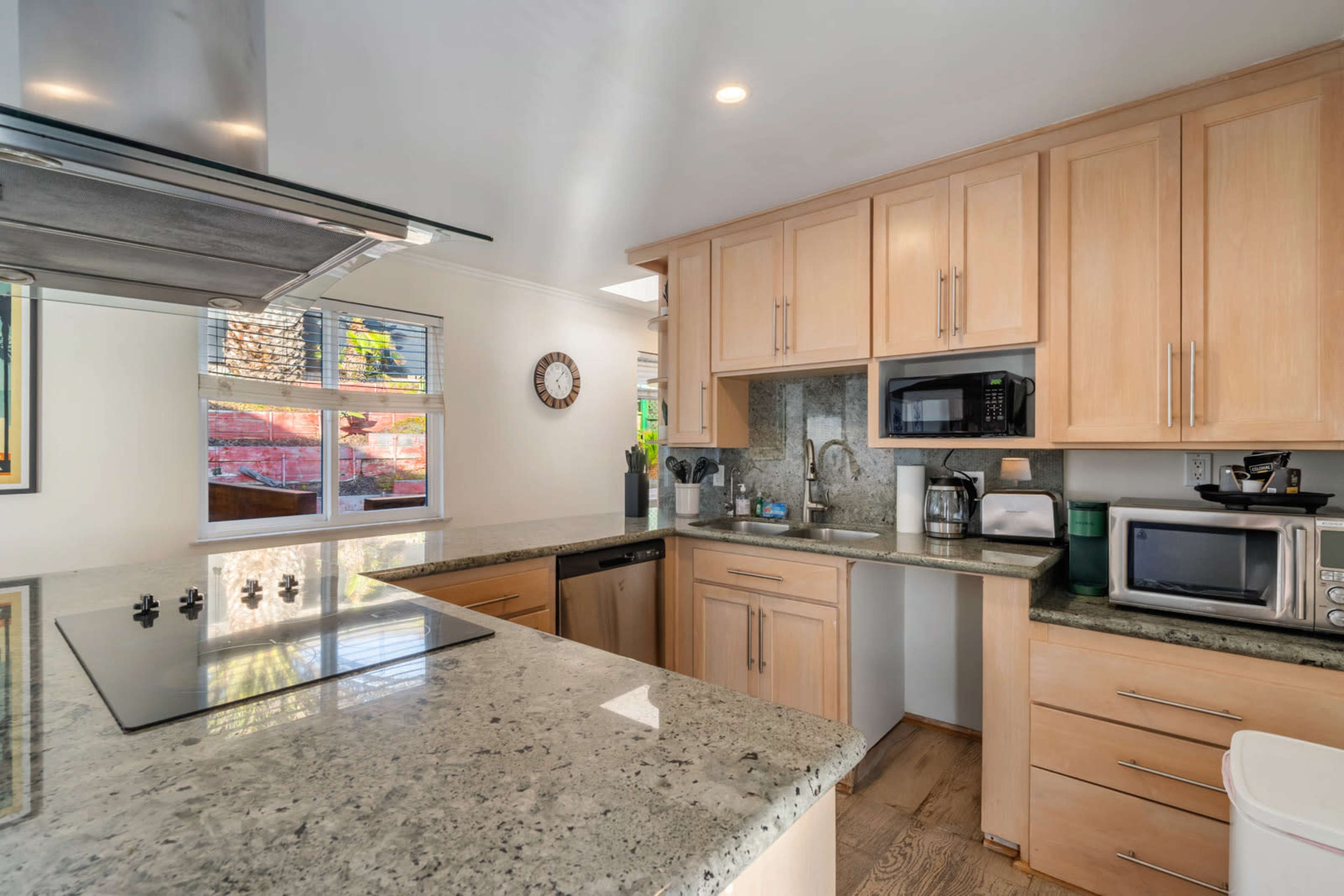 The image shows a modern kitchen featuring light wood cabinets, a granite countertop, and various kitchen appliances.