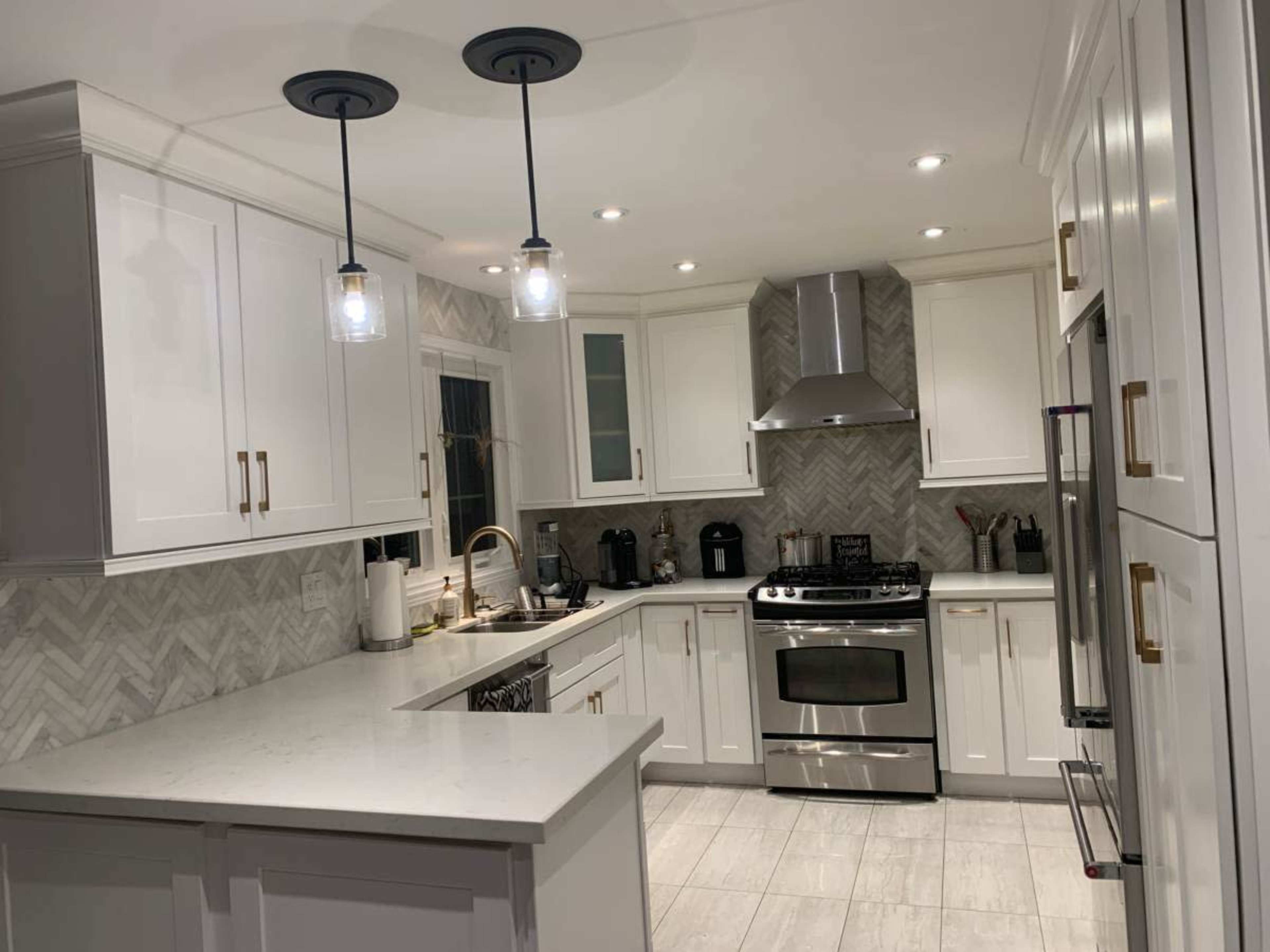The image shows a modern kitchen with white cabinets, a stainless steel stove, and gray chevron-patterned backsplash.