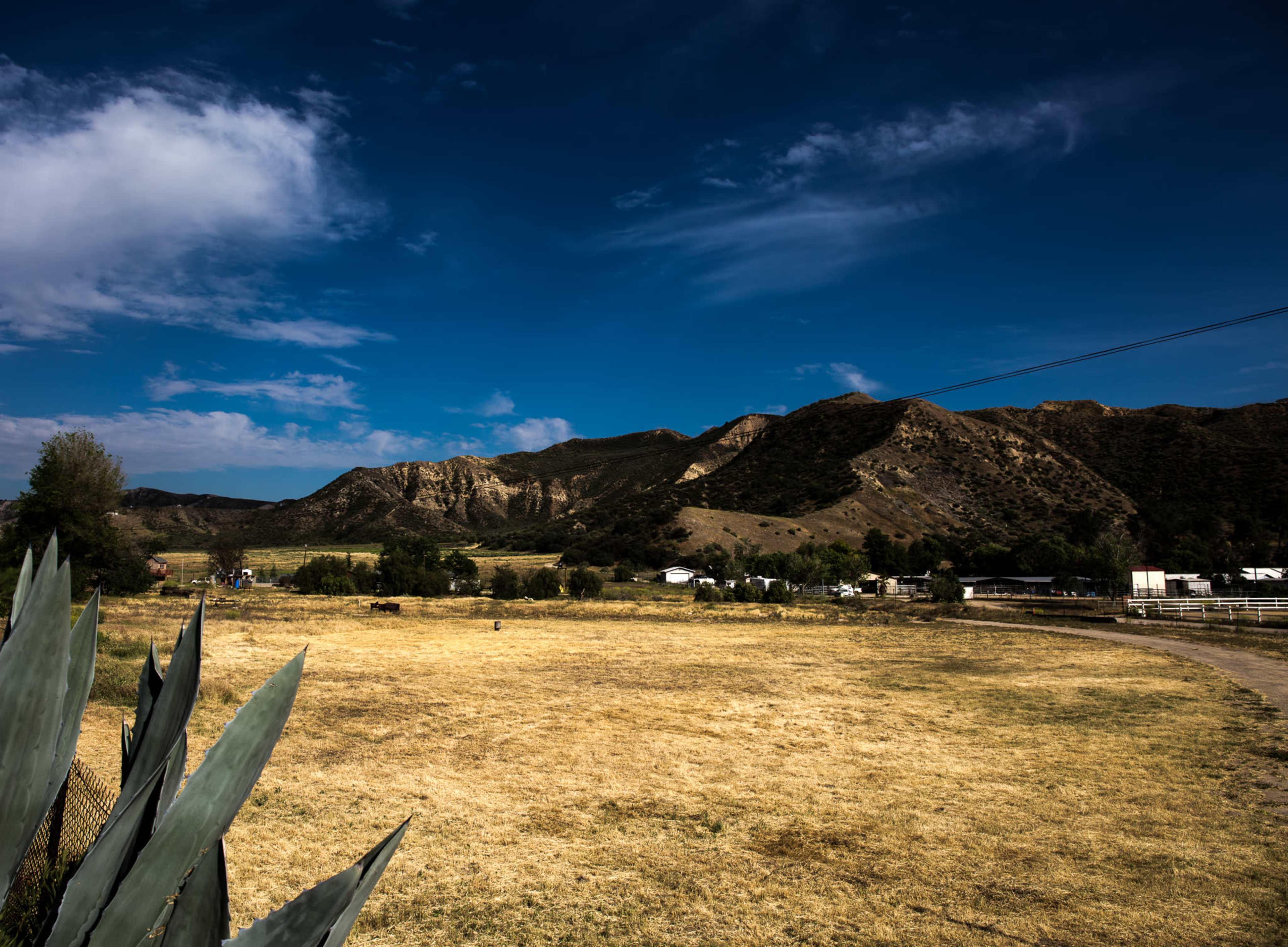 The image shows a grassy field bordered by mountains under a partly cloudy sky.