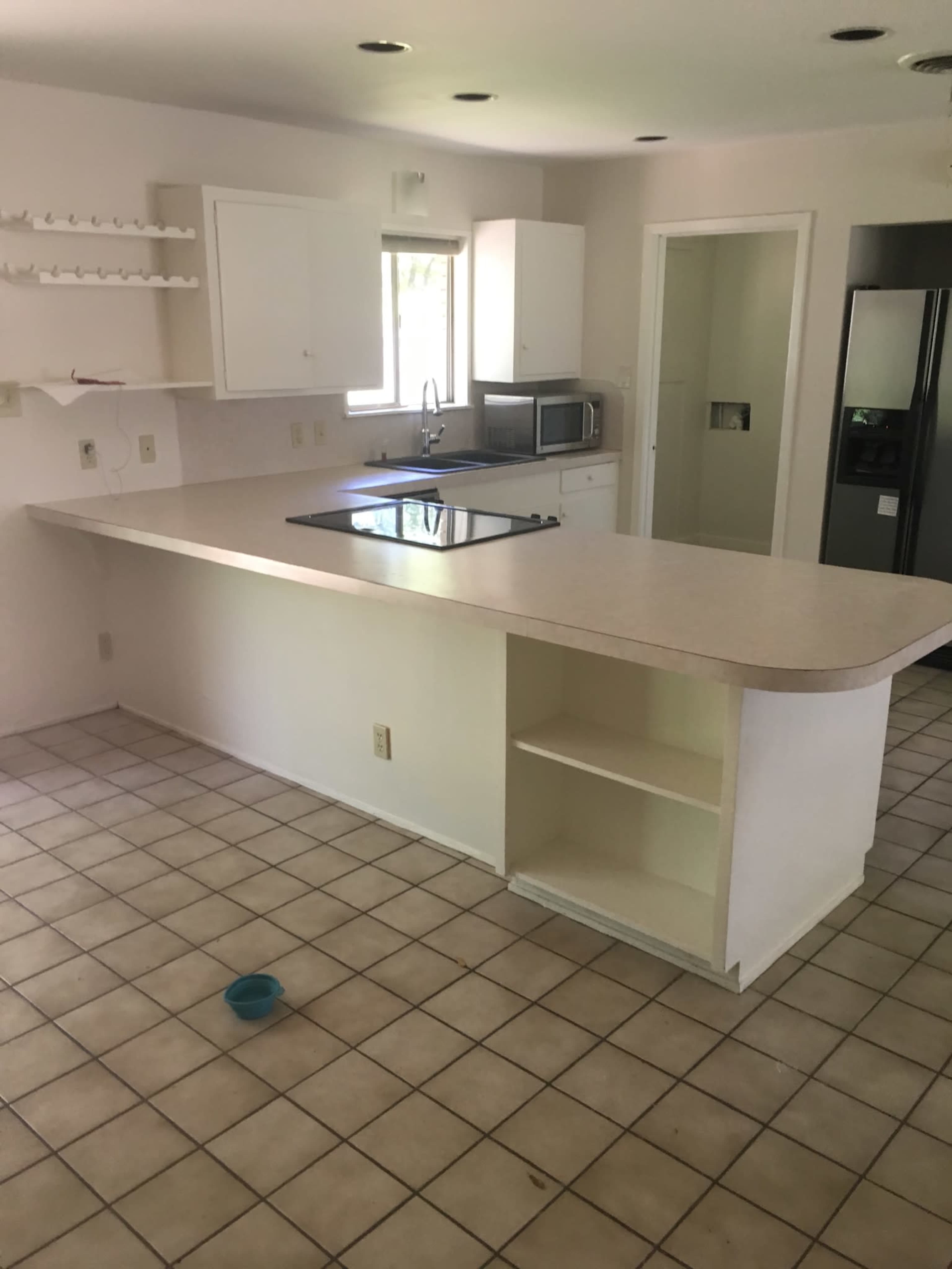 A kitchen with a tile floor, an island with a cooktop, and white cabinetry, is visible, featuring a microwave and refrigerator.
