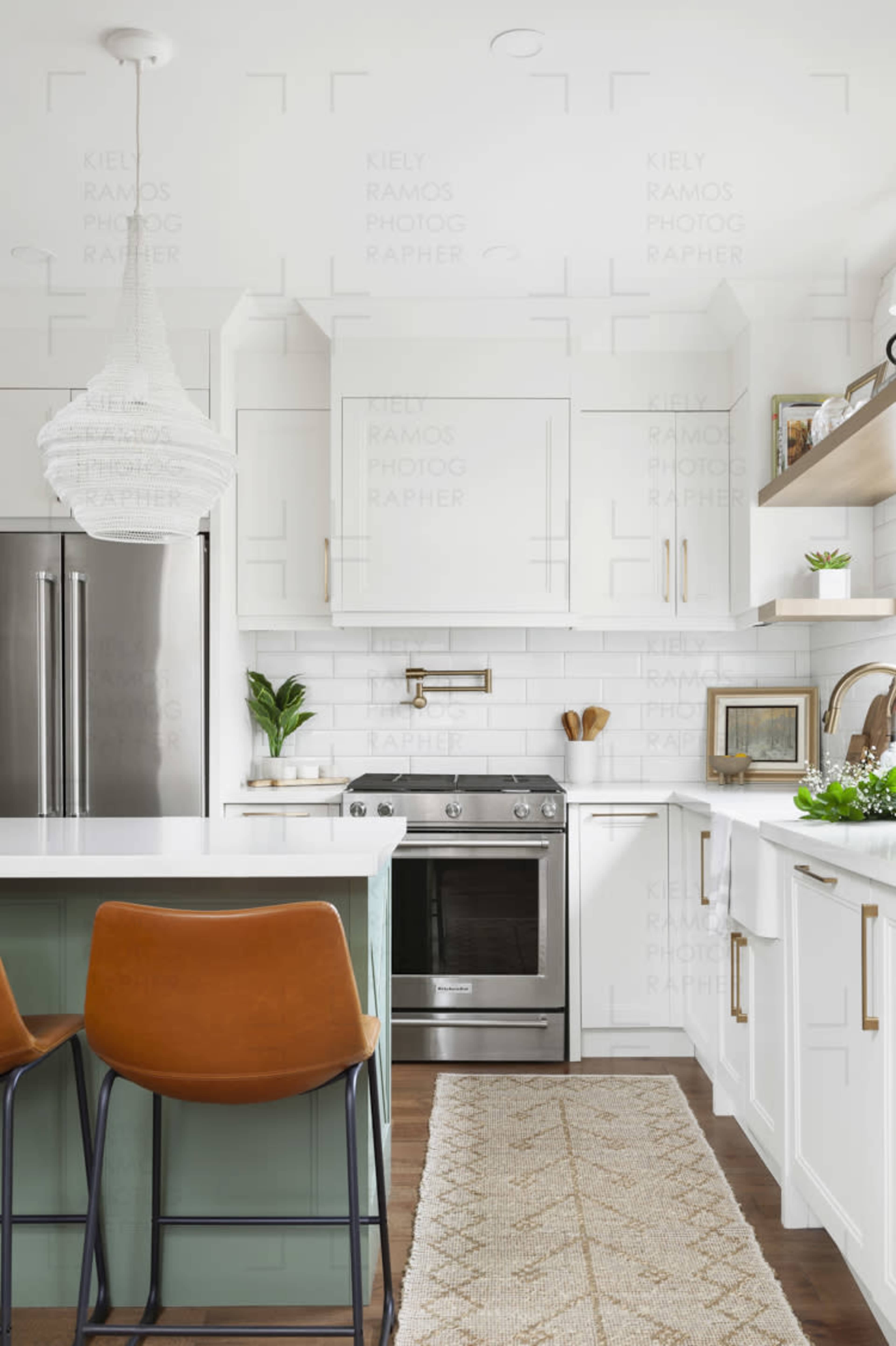 A modern kitchen with white cabinets, stainless steel appliances, and a green island with two brown bar stools.