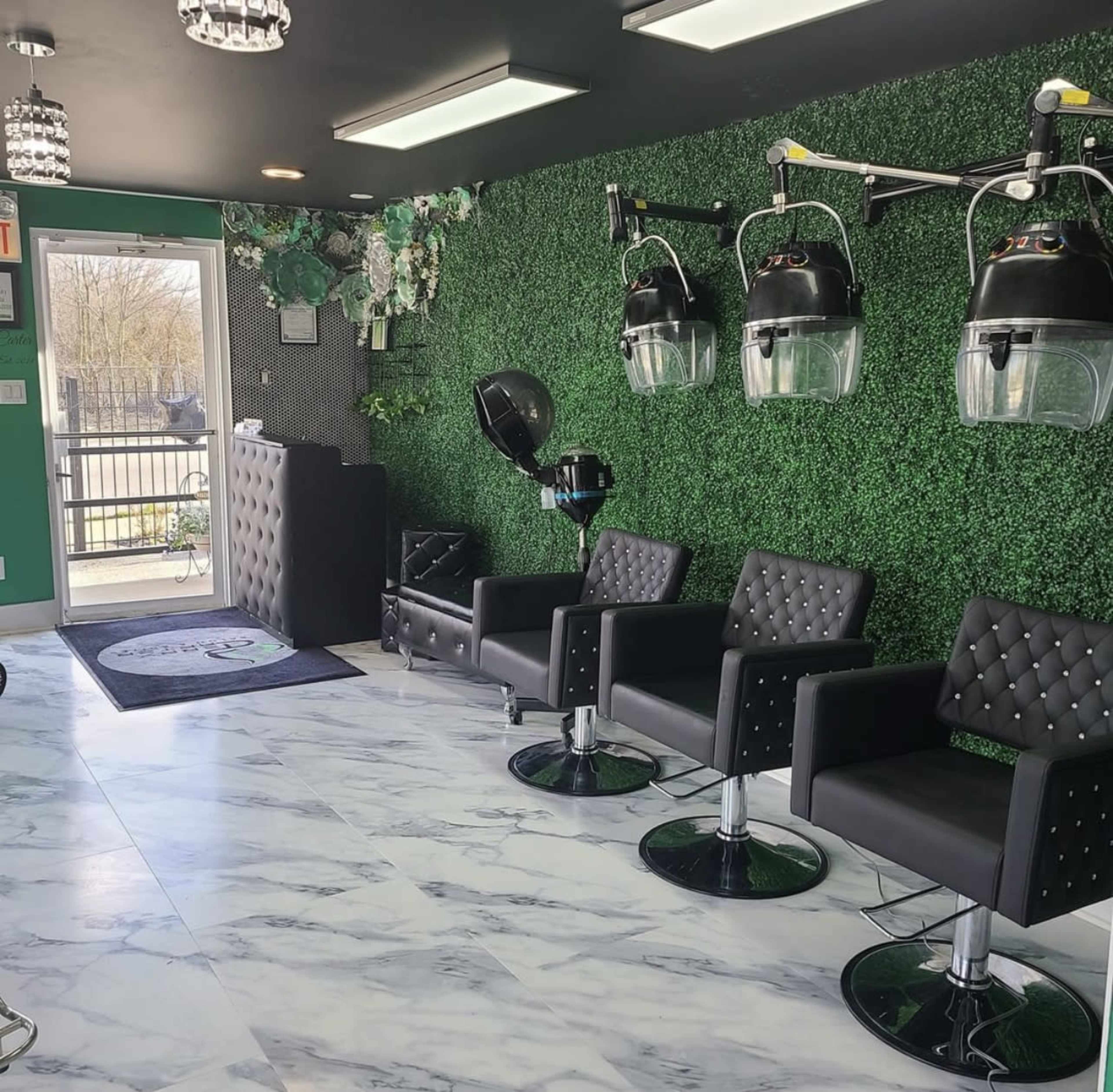 A modern salon interior with black leather chairs, a green plant wall, and hooded hair dryers on stands.