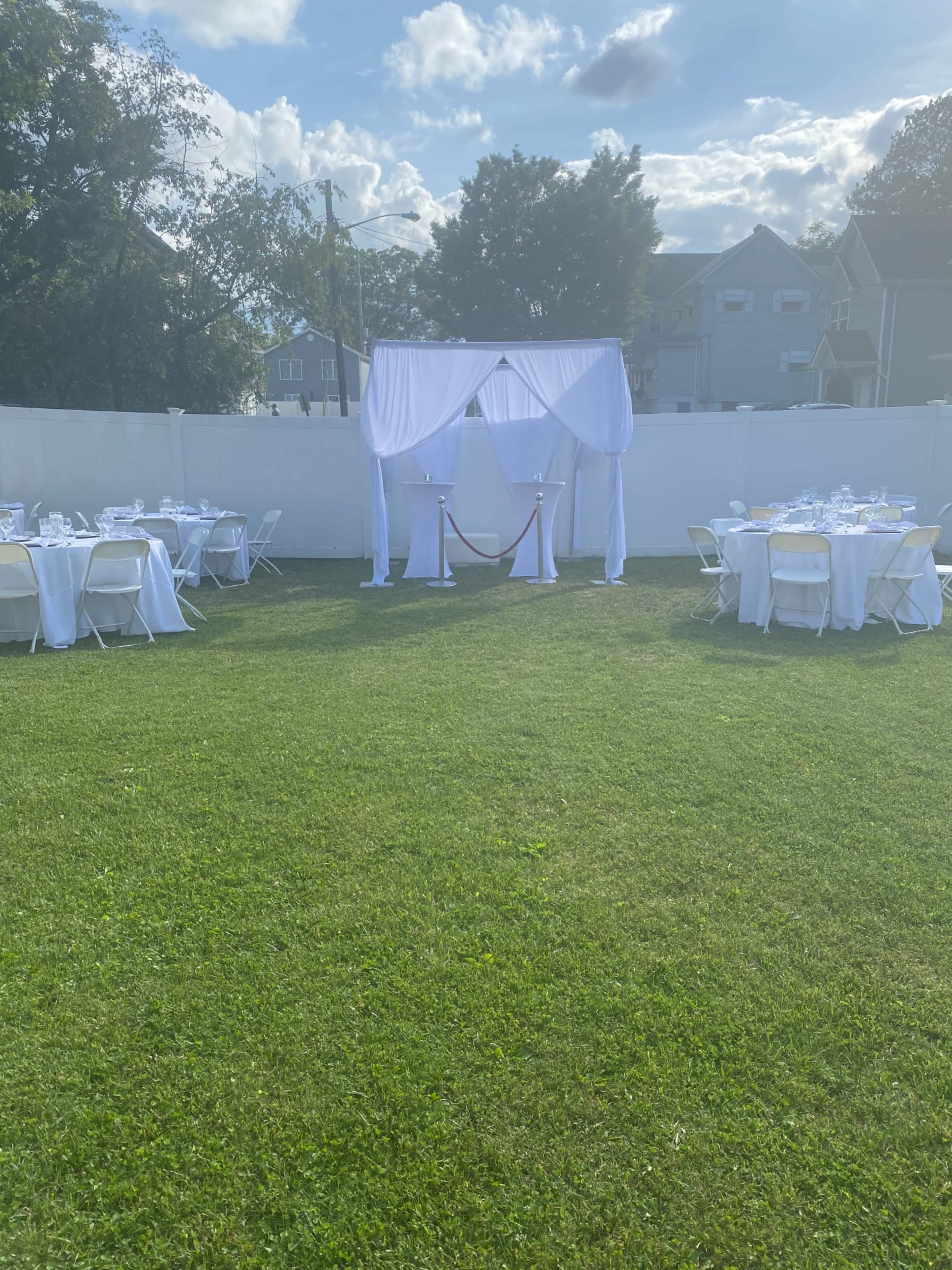 A tented altar stands in a grassy area surrounded by white table settings for an outdoor event.