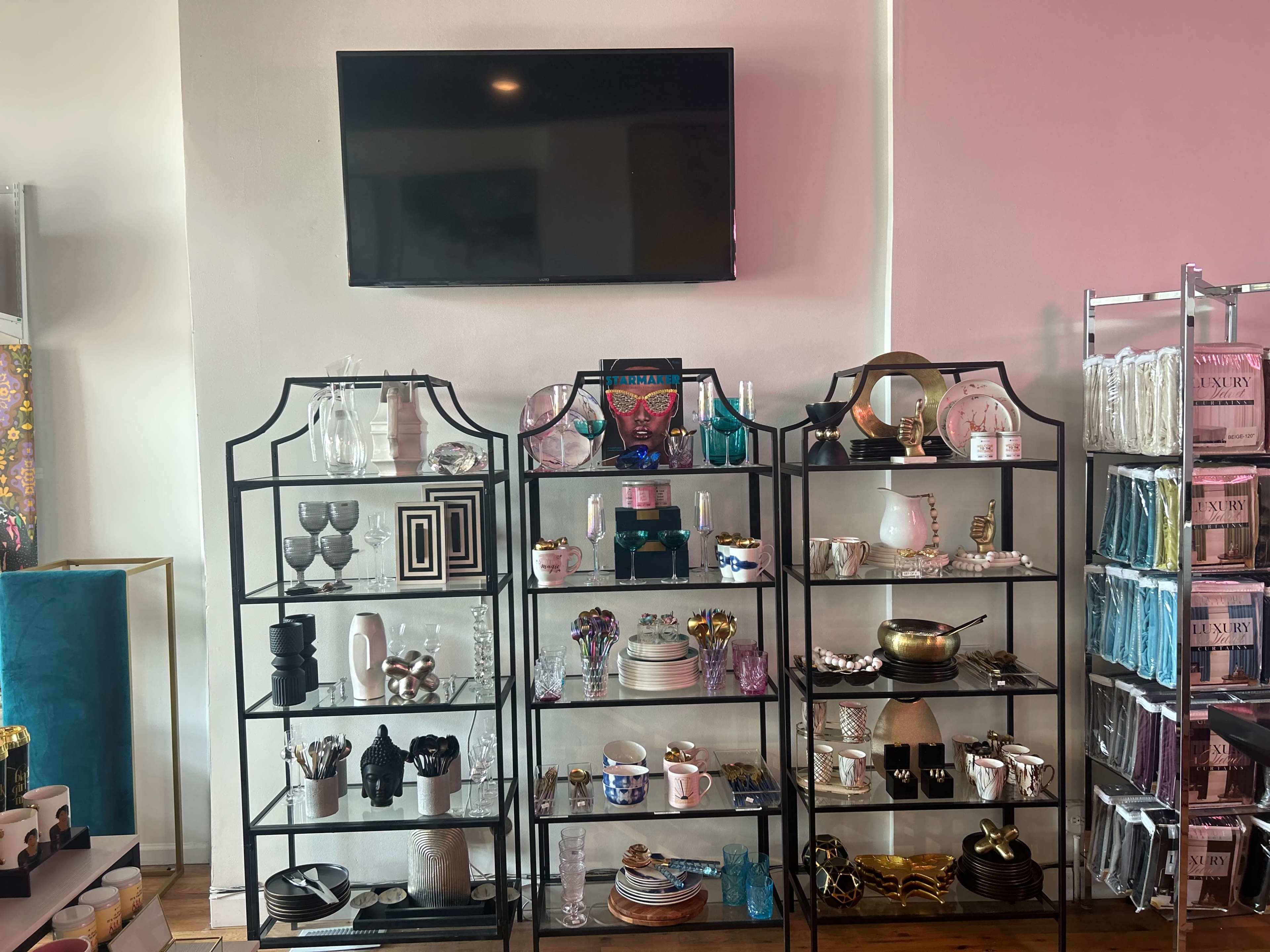 Two metal display shelves filled with a variety of glassware, ceramics, and decorative items, with a television mounted on the wall above.