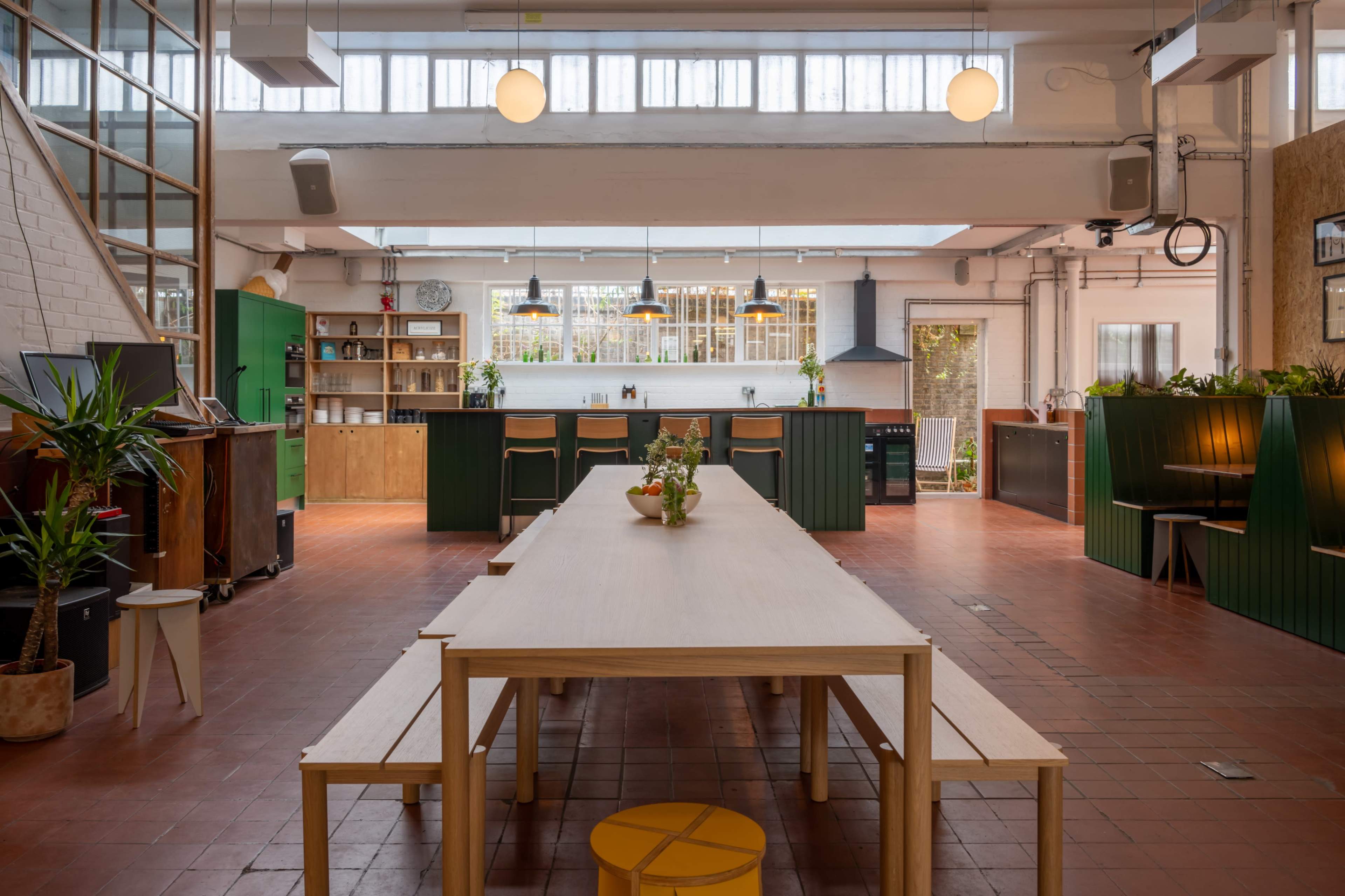 A spacious kitchen and dining area with a long wooden table, benches, green cabinetry, and large windows allowing natural light to fill the space.