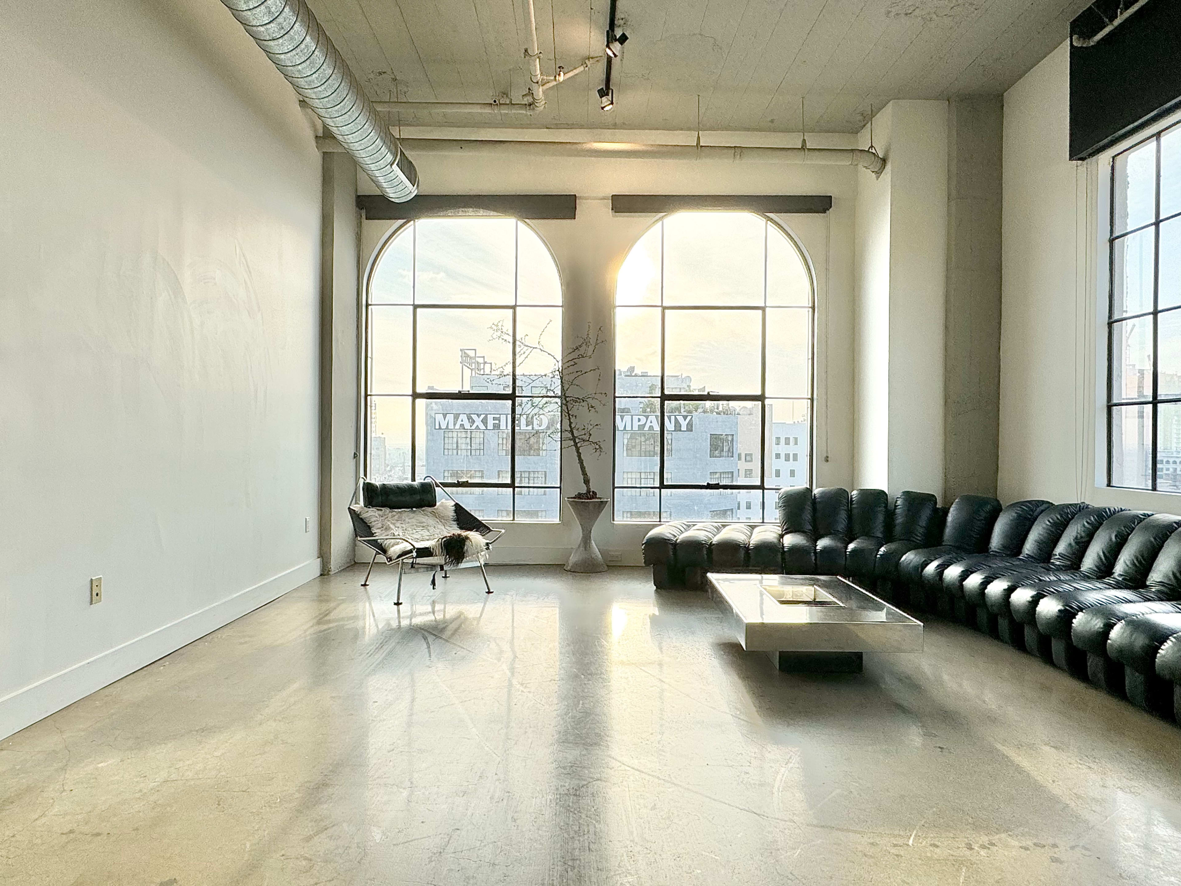 A spacious room with large arched windows, featuring a black leather sofa, a glass coffee table, and minimal decor.