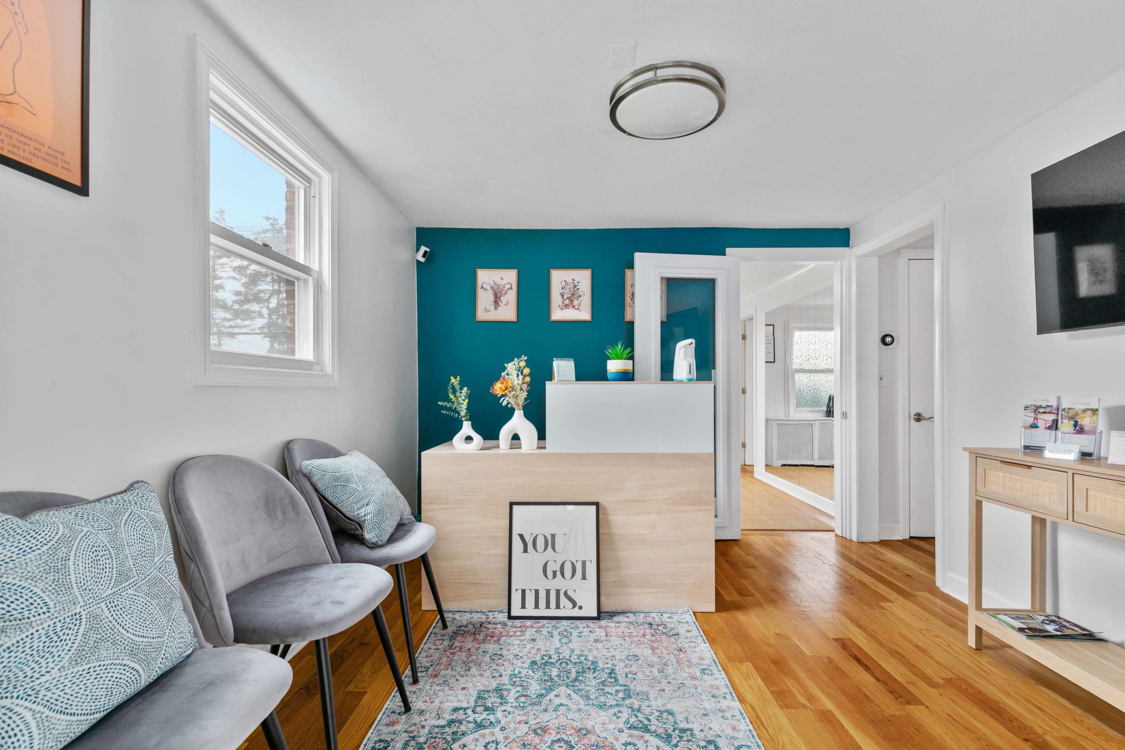 A bright reception area featuring a wooden front desk, gray chairs, and teal accent walls adorned with framed artwork.