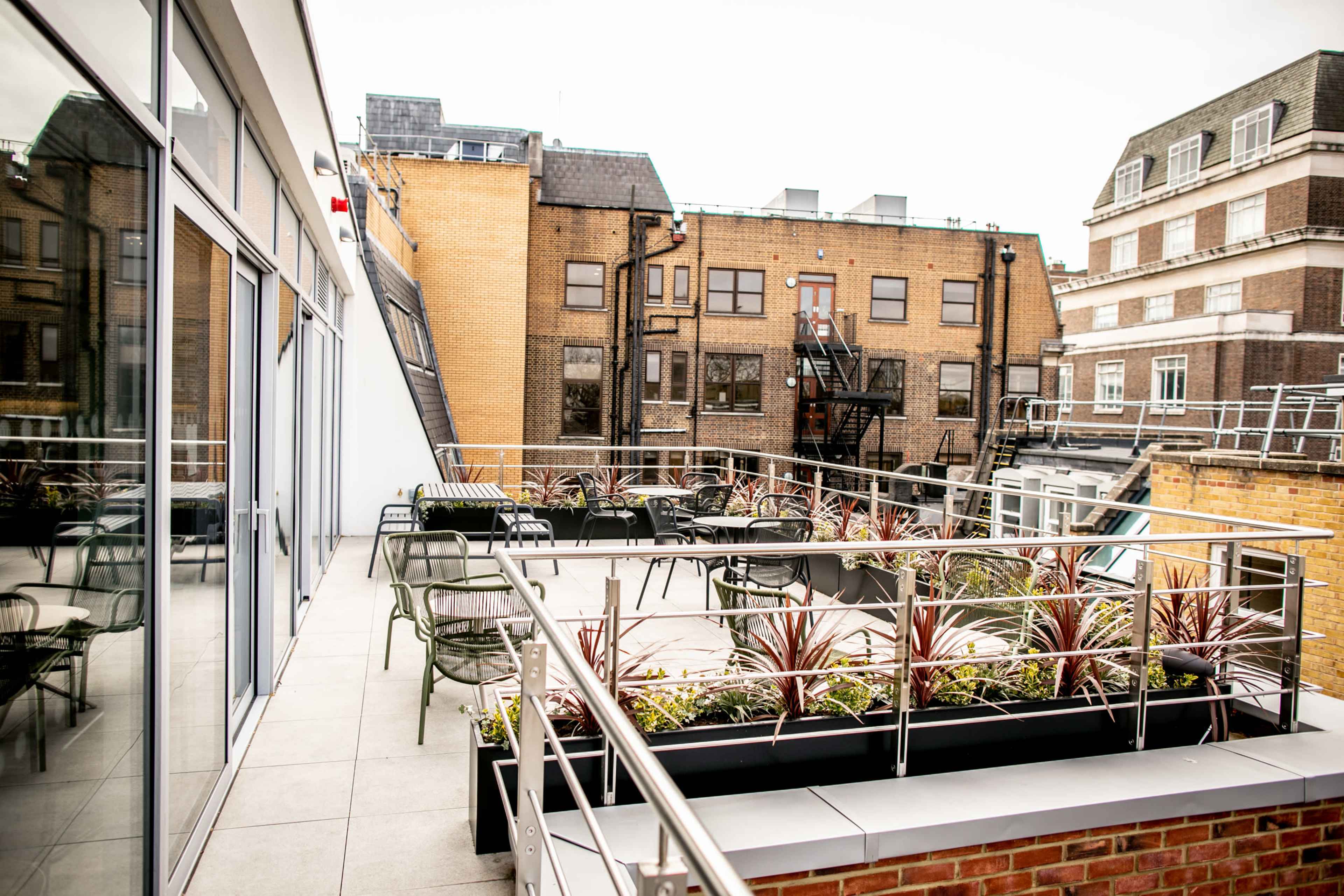 A rooftop terrace with seating and planters surrounded by neighboring buildings.