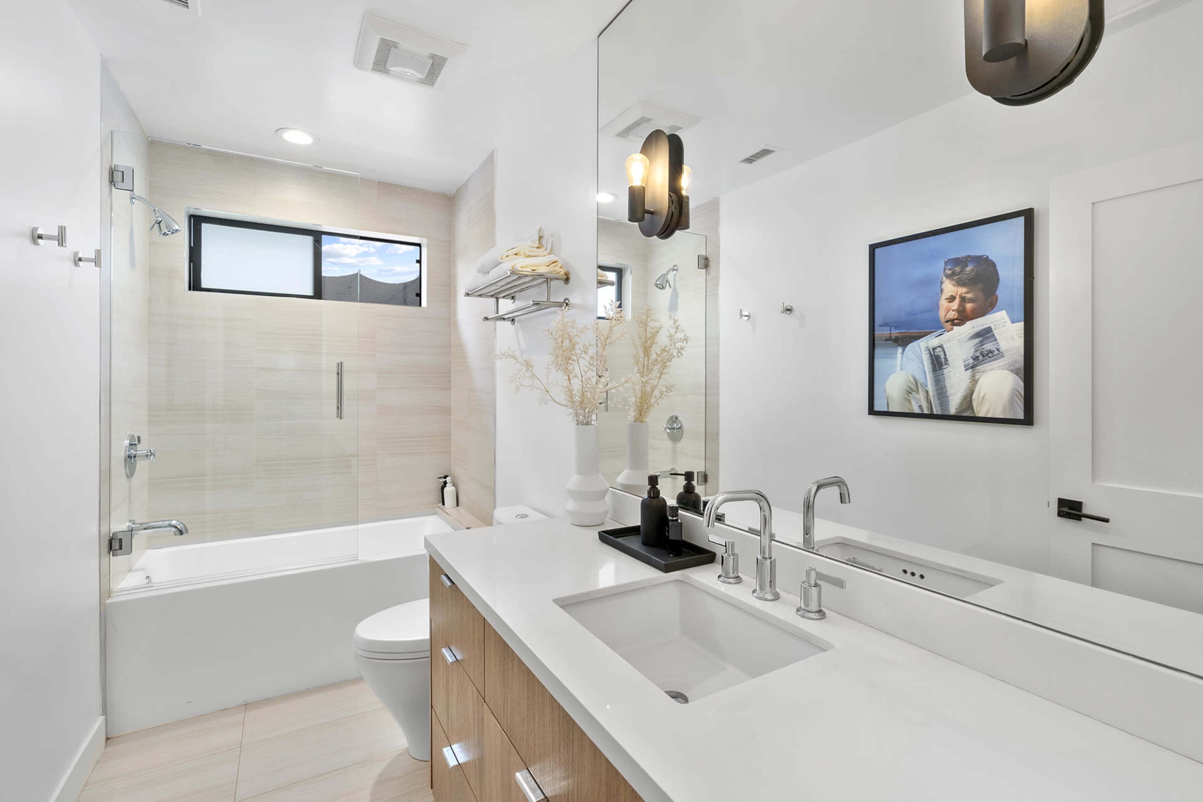The modern bathroom features a tub and shower combination, a double vanity with wooden cabinetry, and a large mirror above the sinks.