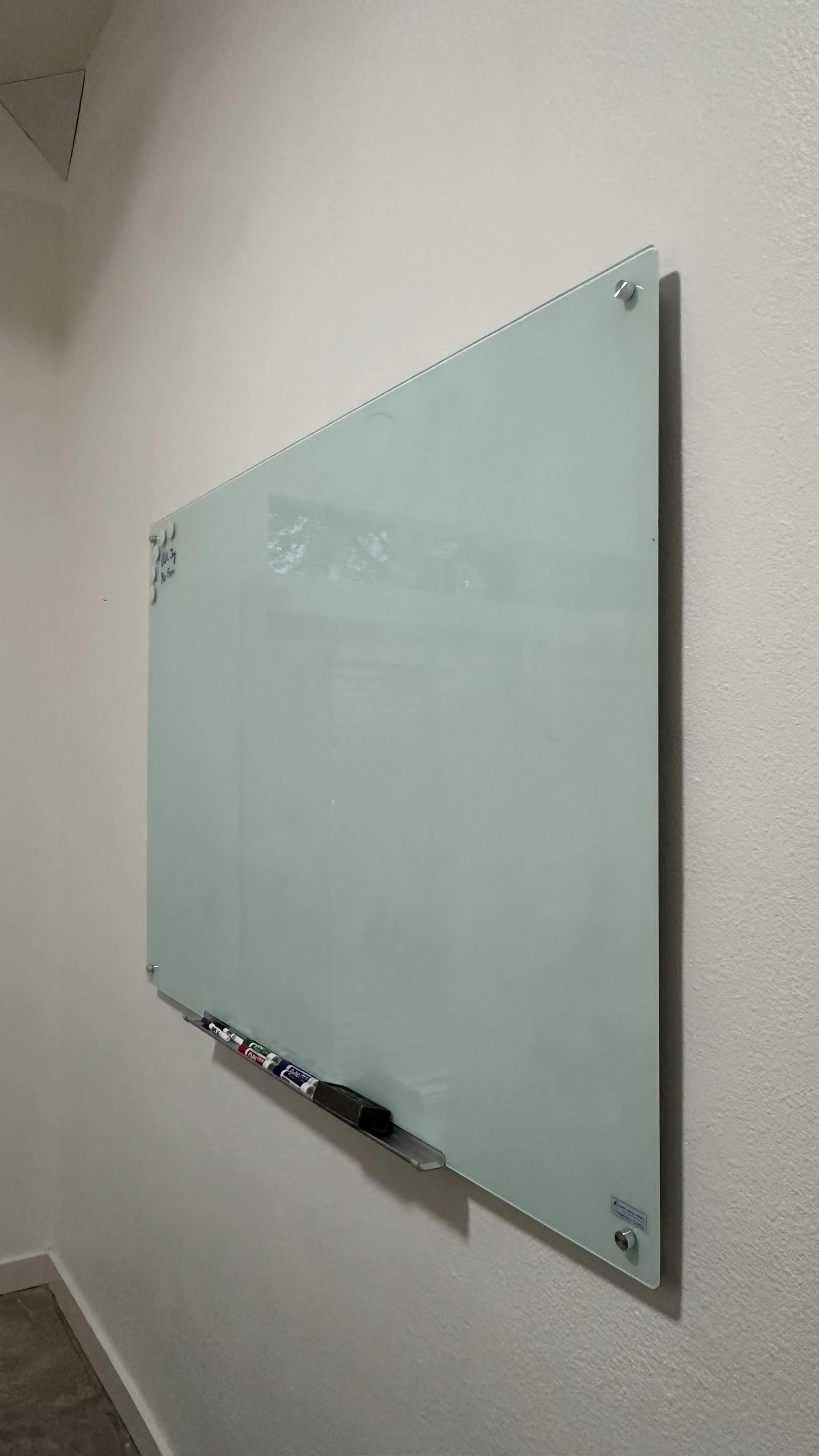A large, clear glass whiteboard is mounted on a light-colored wall.