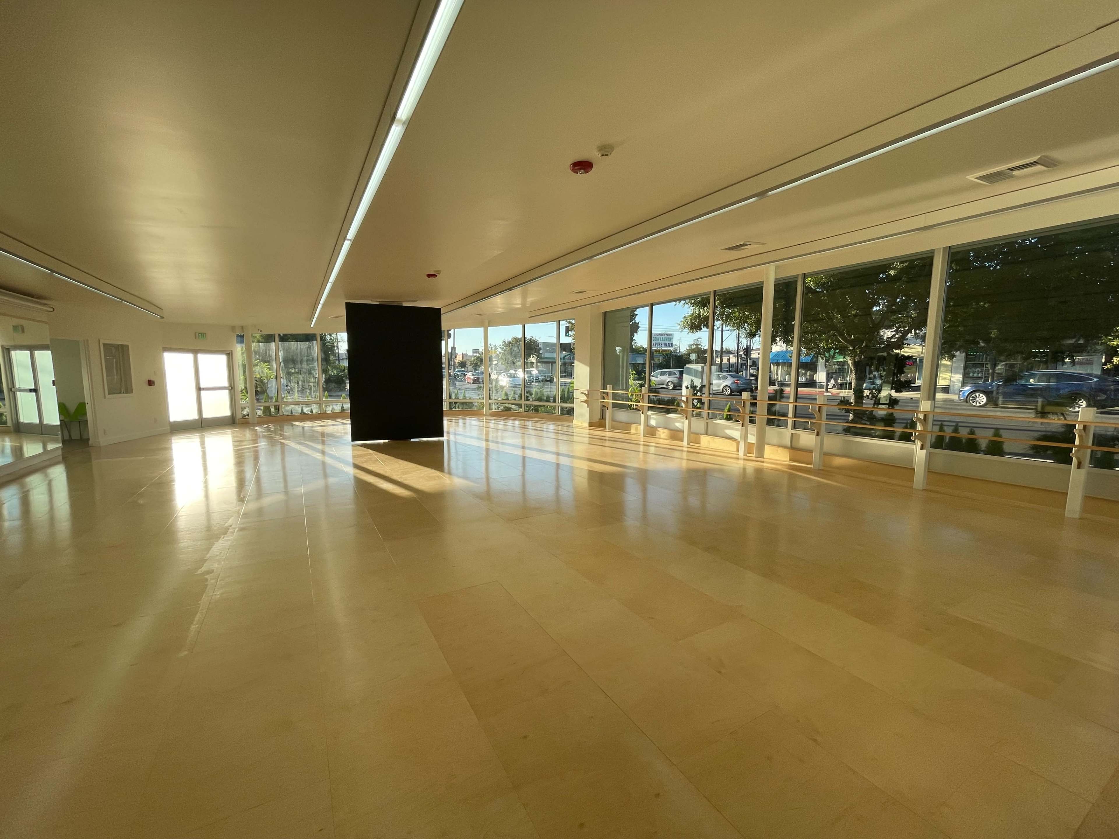 A spacious, empty room with large windows and a black partition in the center, illuminated by natural light.