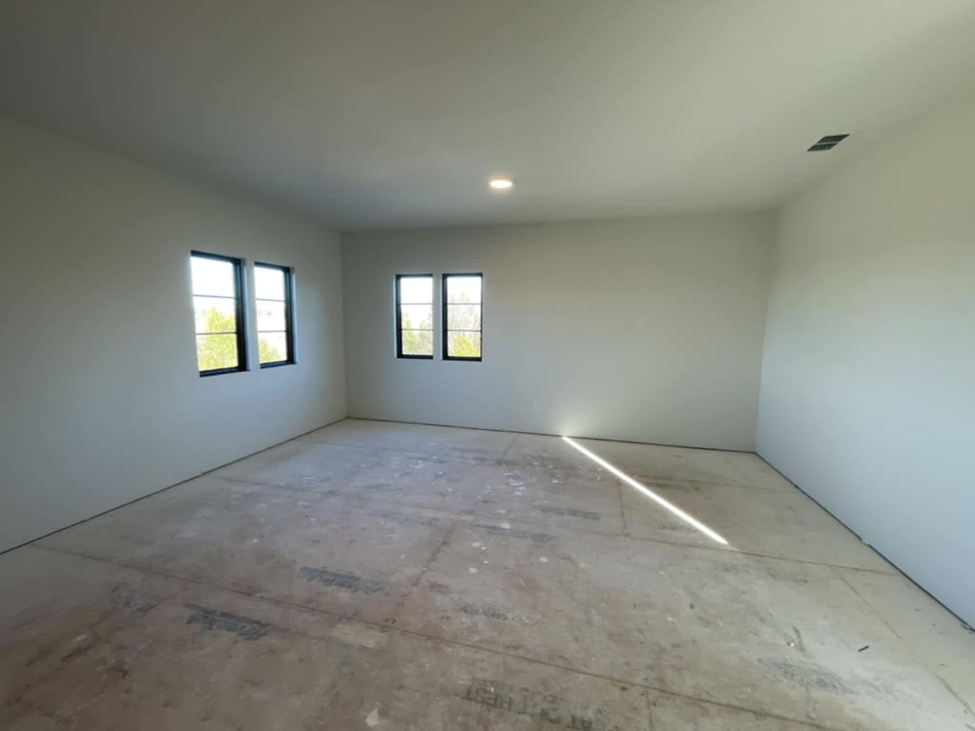 An empty room with unpainted walls, three windows, and a bare floor.