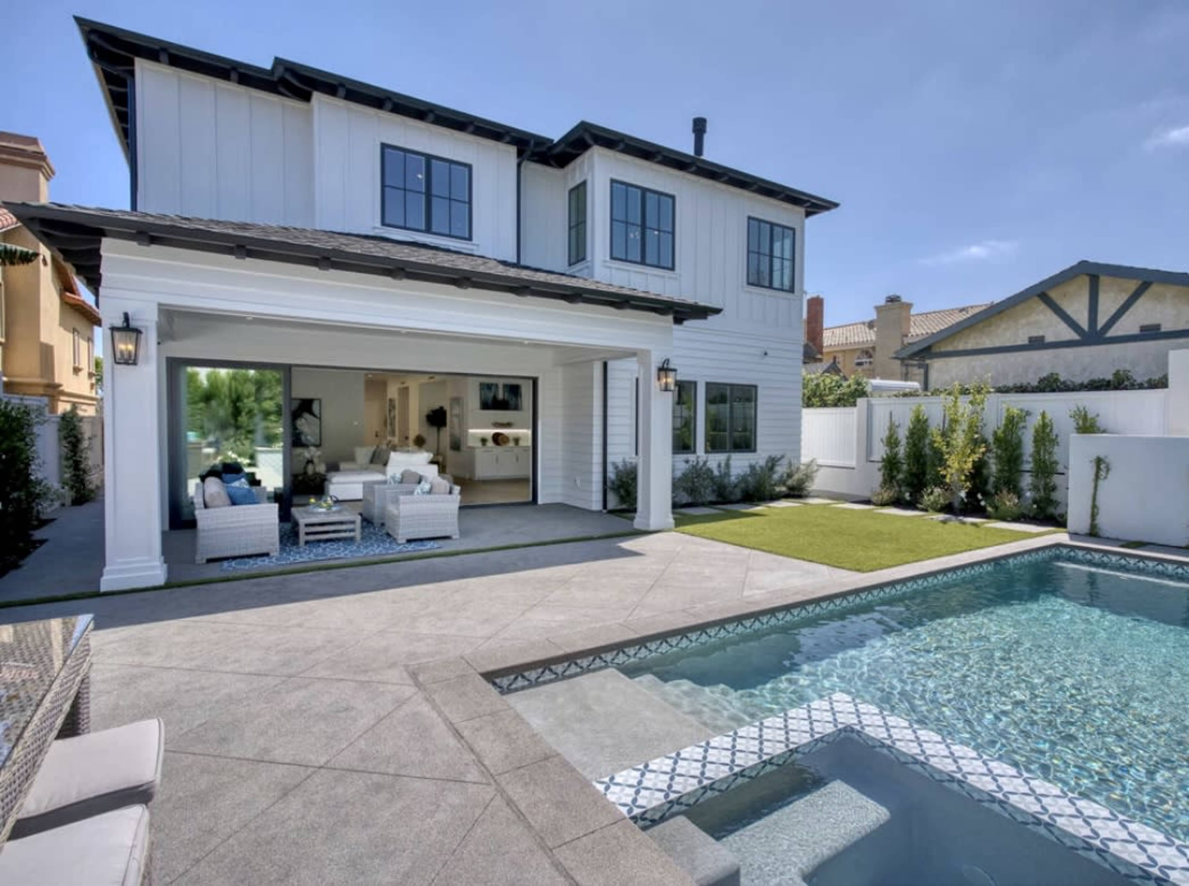 A modern two-story house with a pool and outdoor seating area in a residential backyard.