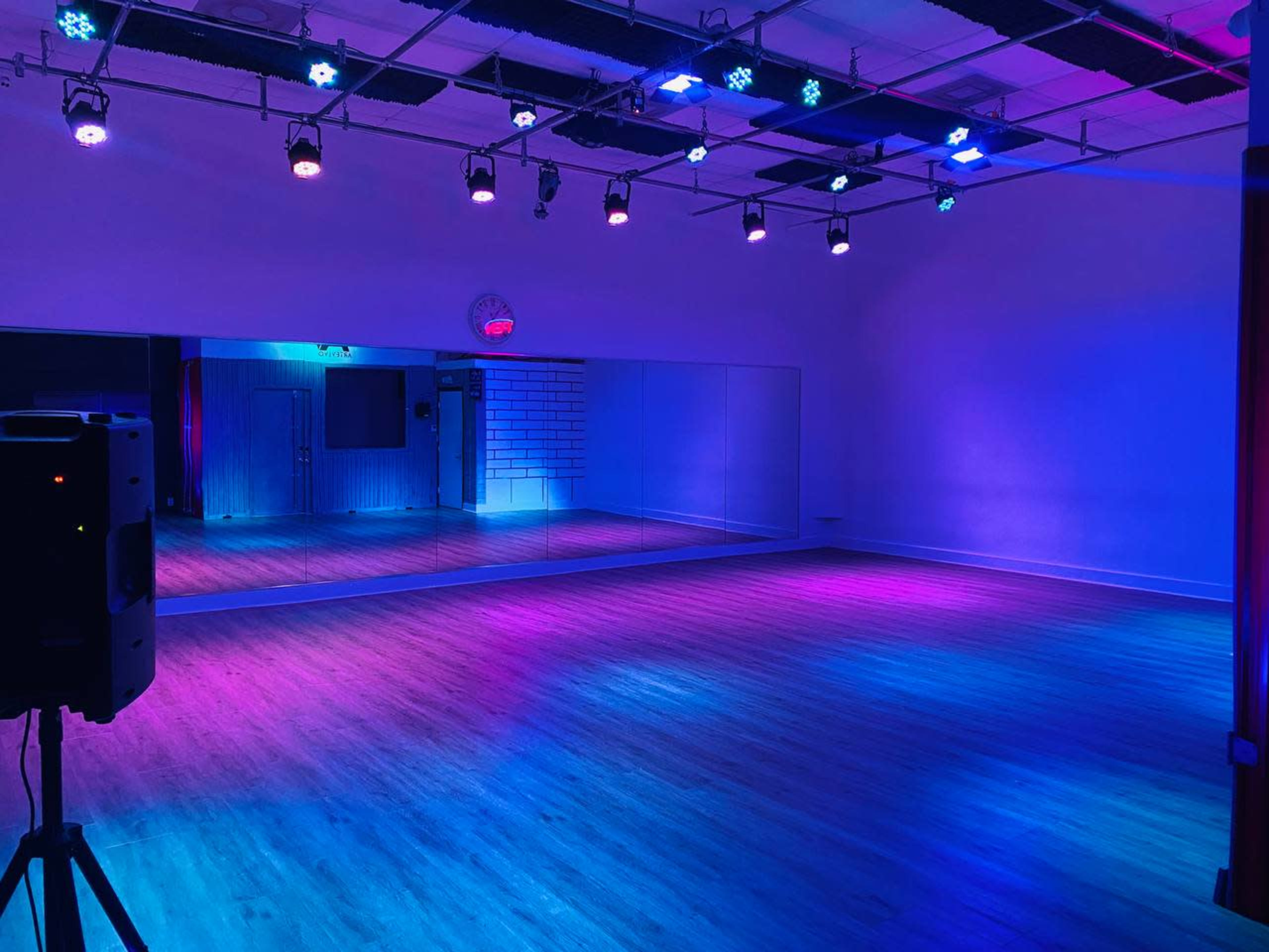 A dance studio with a large mirror wall, illuminated by colorful LED lights and wooden flooring.