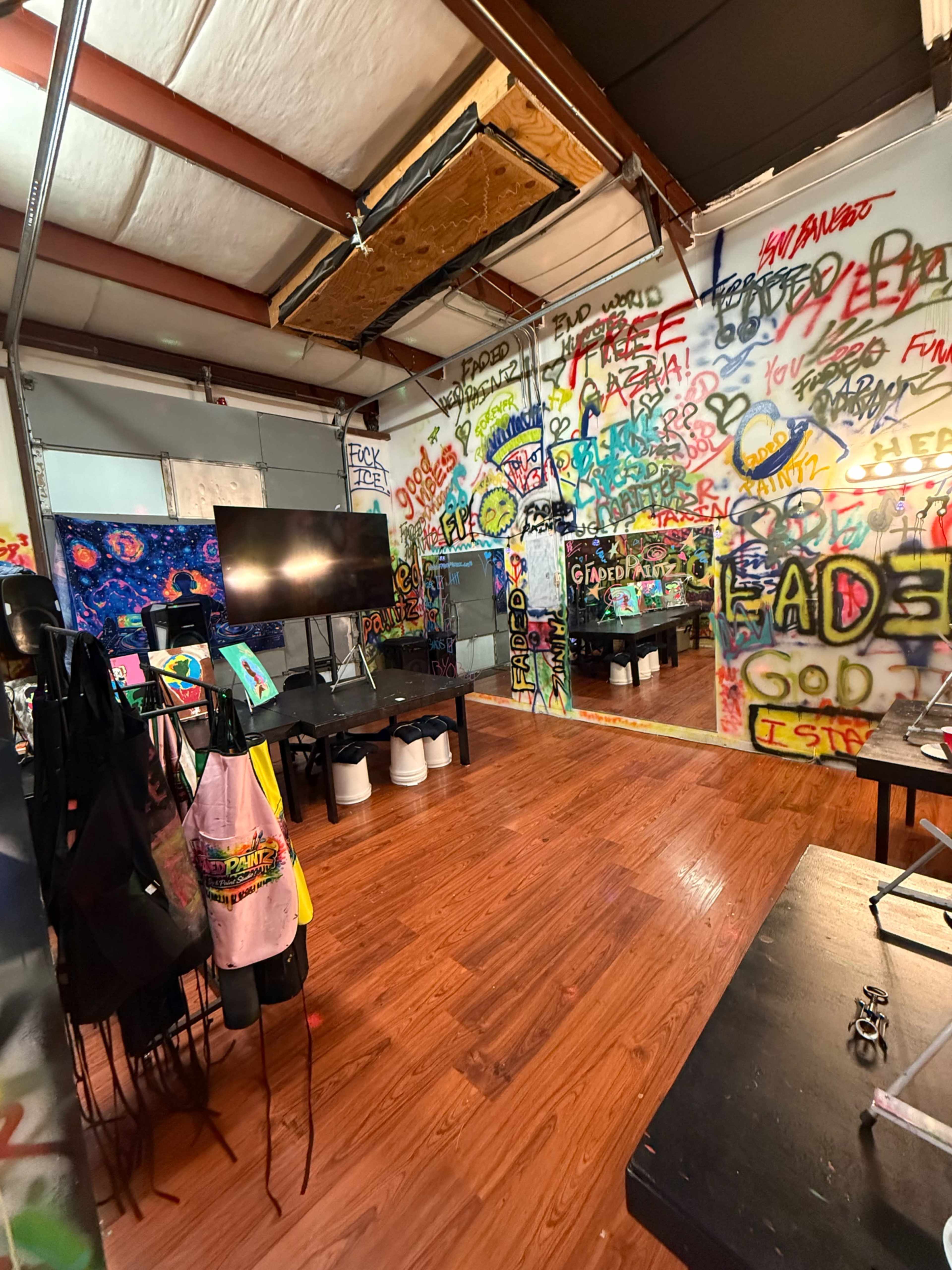 The room features colorful graffiti covering the walls, a television mounted on a nearby wall, and various art supplies arranged on tables.