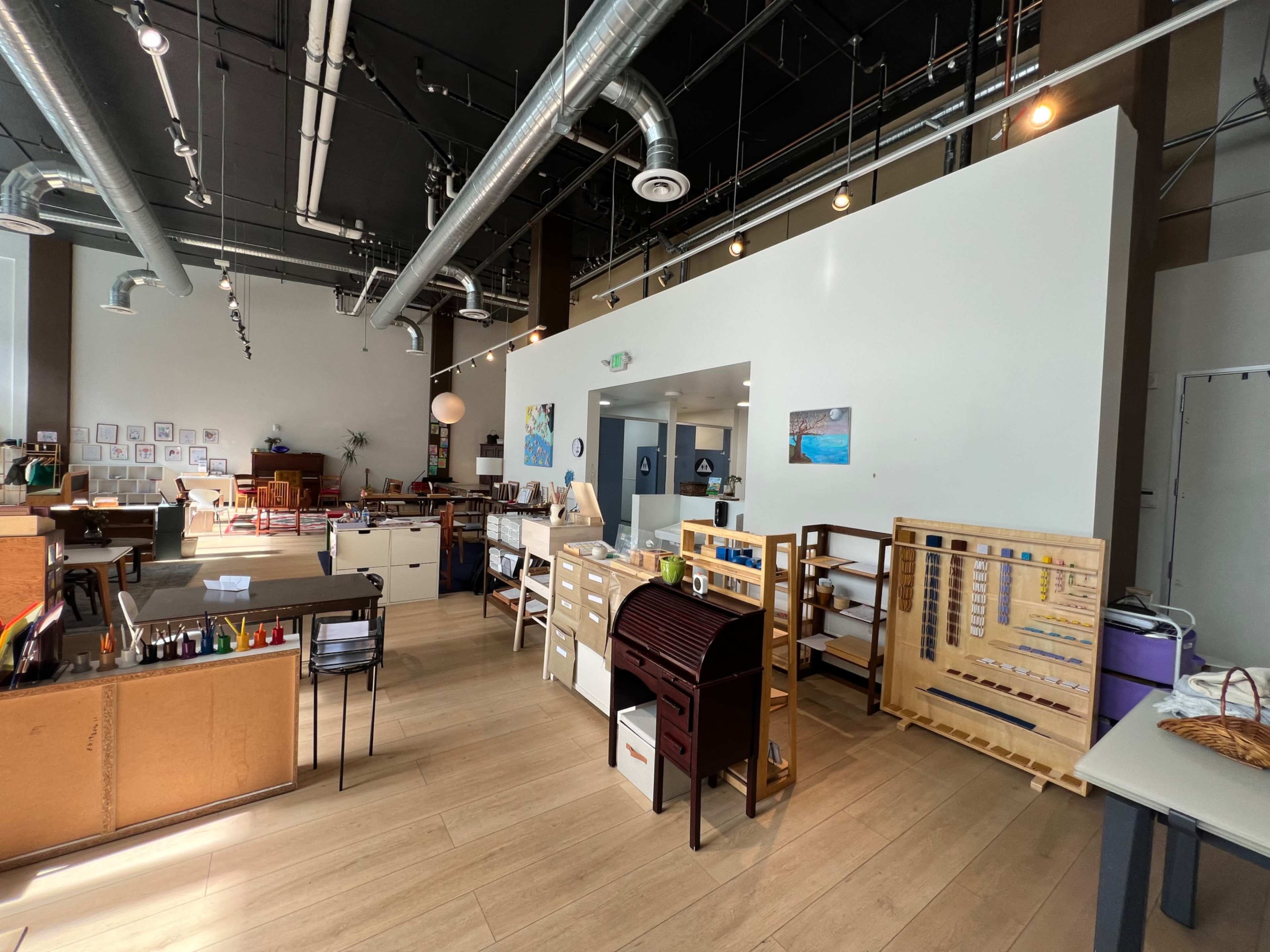 The image shows a spacious art studio with various workstations, storage units, and large windows allowing natural light to enter.