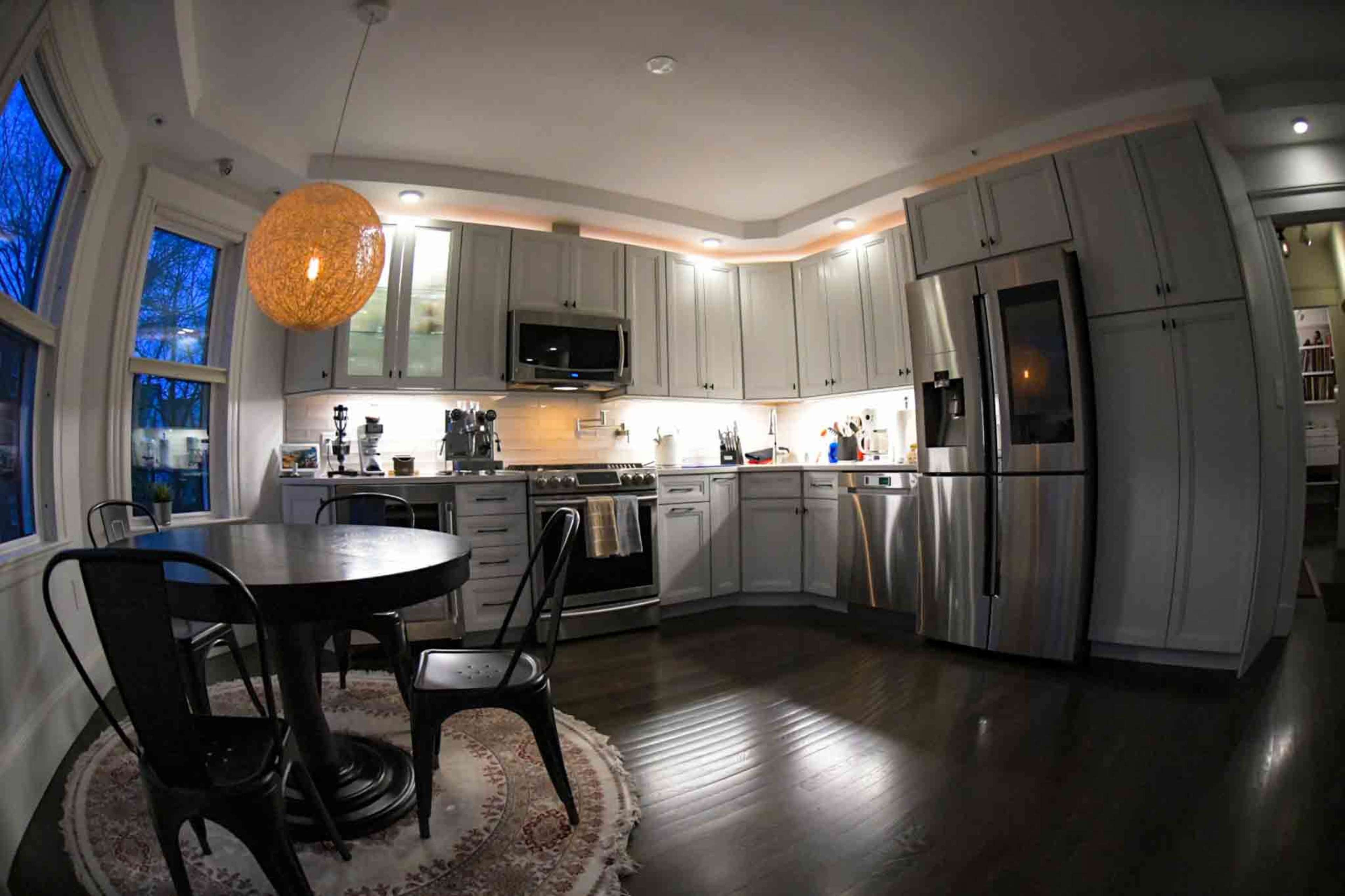 A modern kitchen features stainless steel appliances, white cabinetry, a round table with black chairs, and a large pendant light.