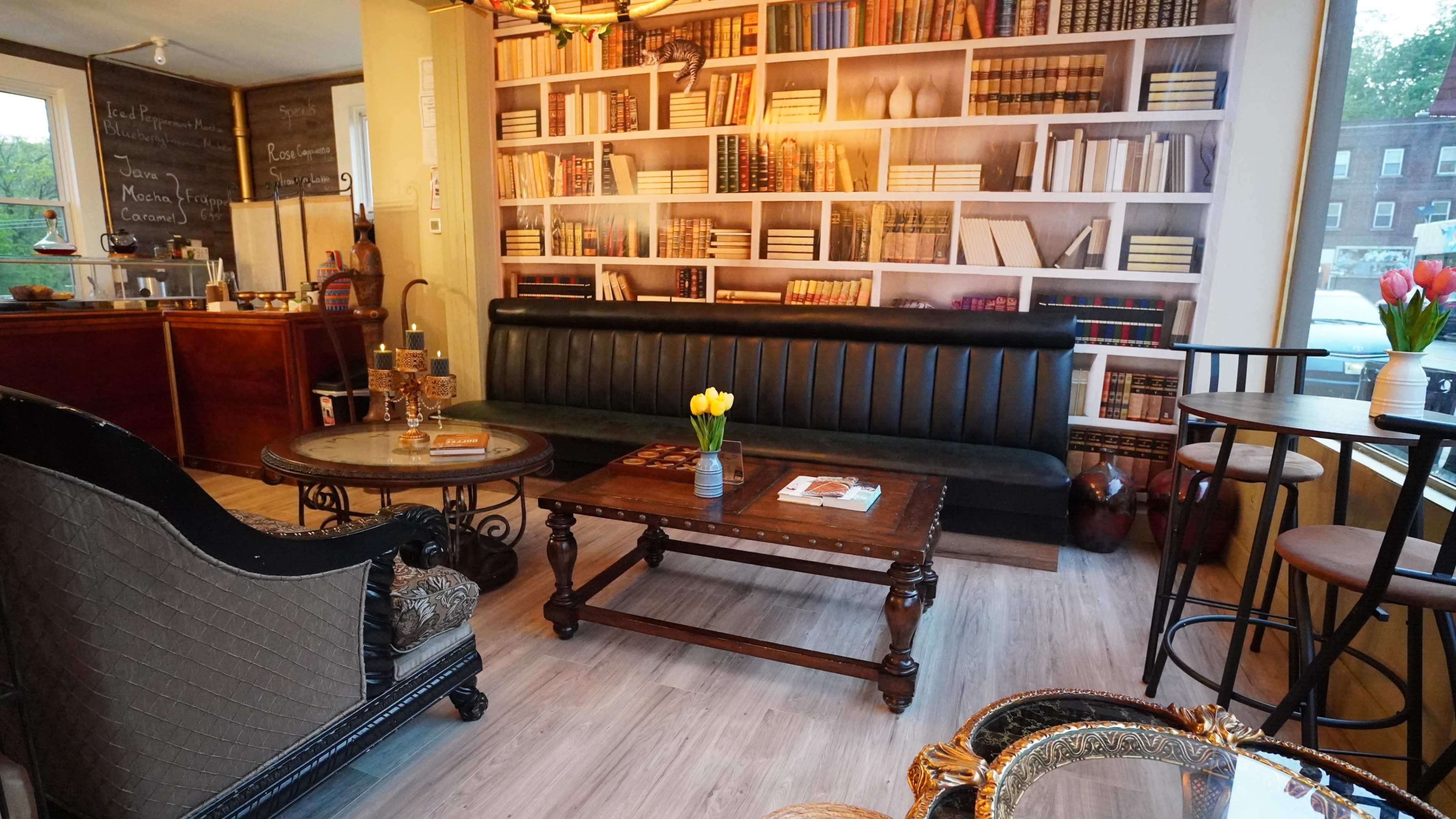 A cozy café interior with a black leather sofa, a wooden coffee table, and bookshelves in the background.