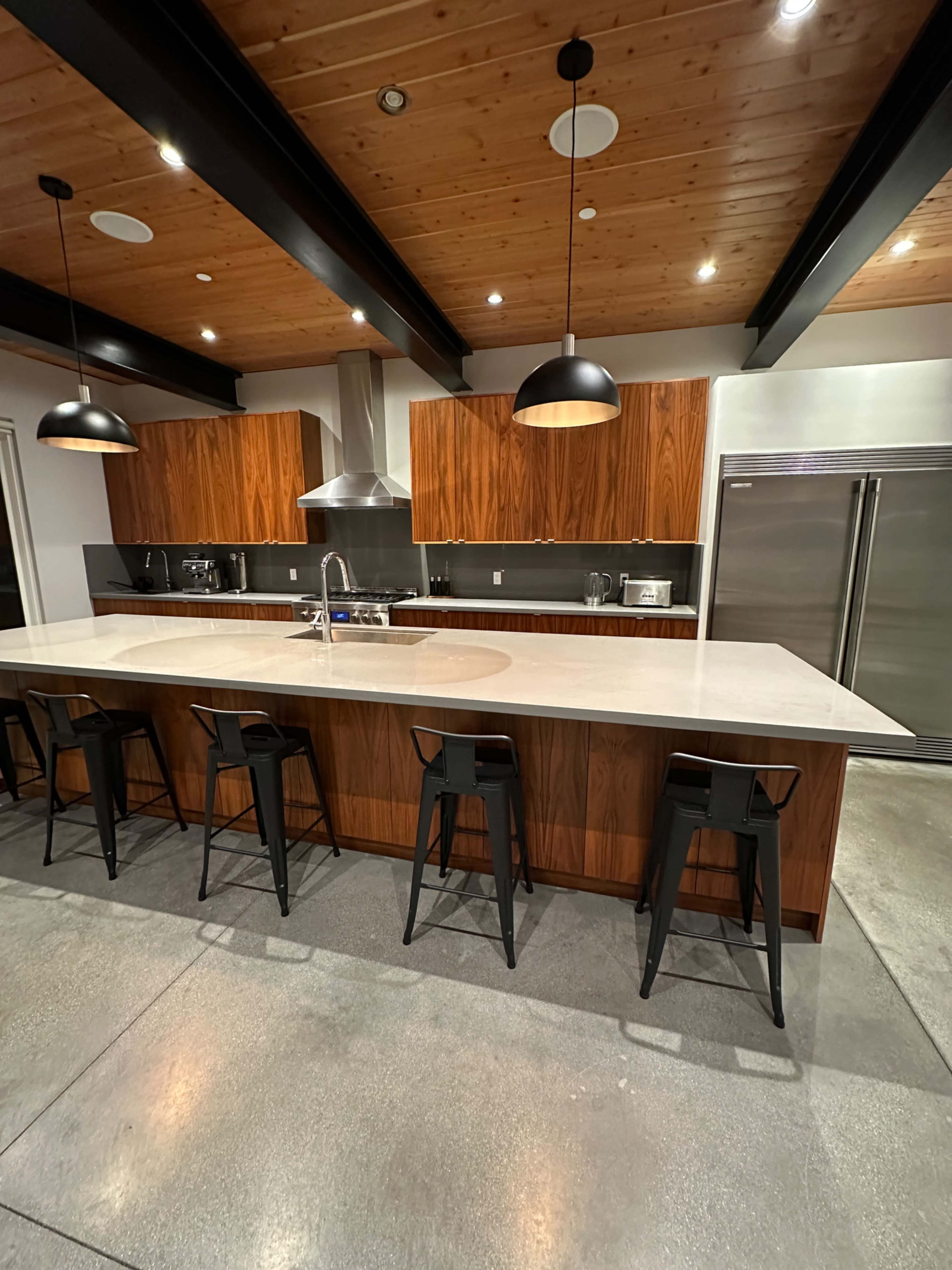 A modern kitchen with a large island, wooden cabinets, stainless steel appliances, and pendant lighting.