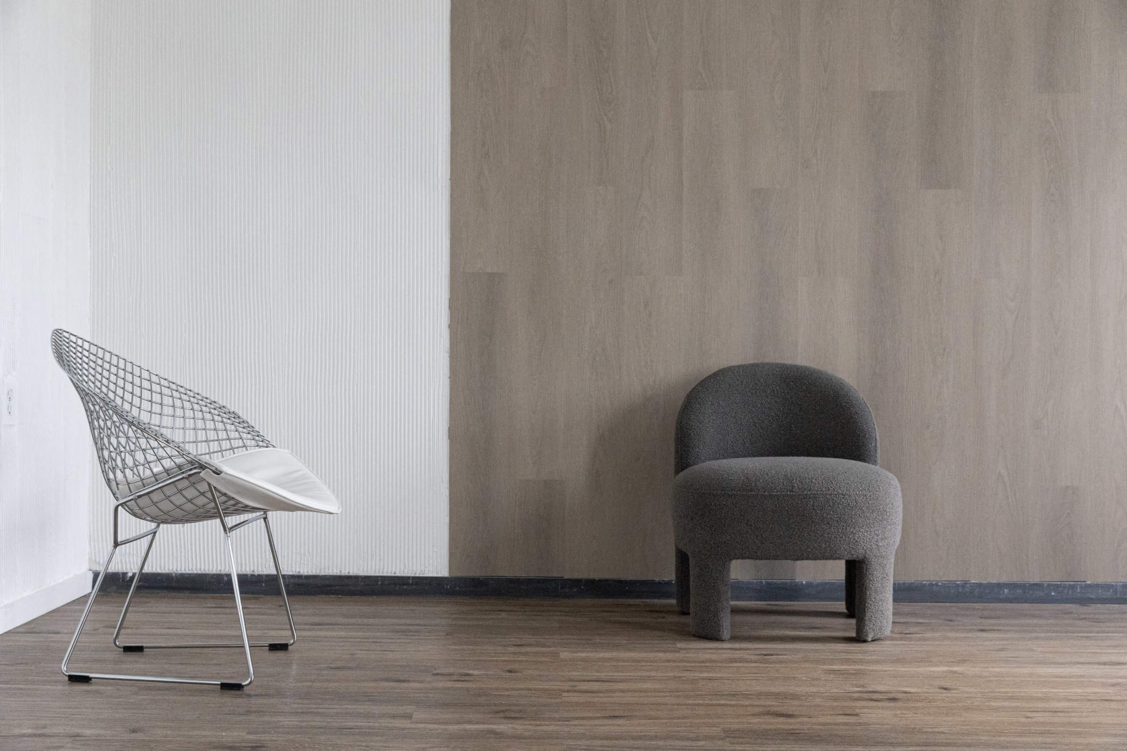 The image features a minimalist interior with a wireframe chair and a rounded upholstered chair on a wooden floor.