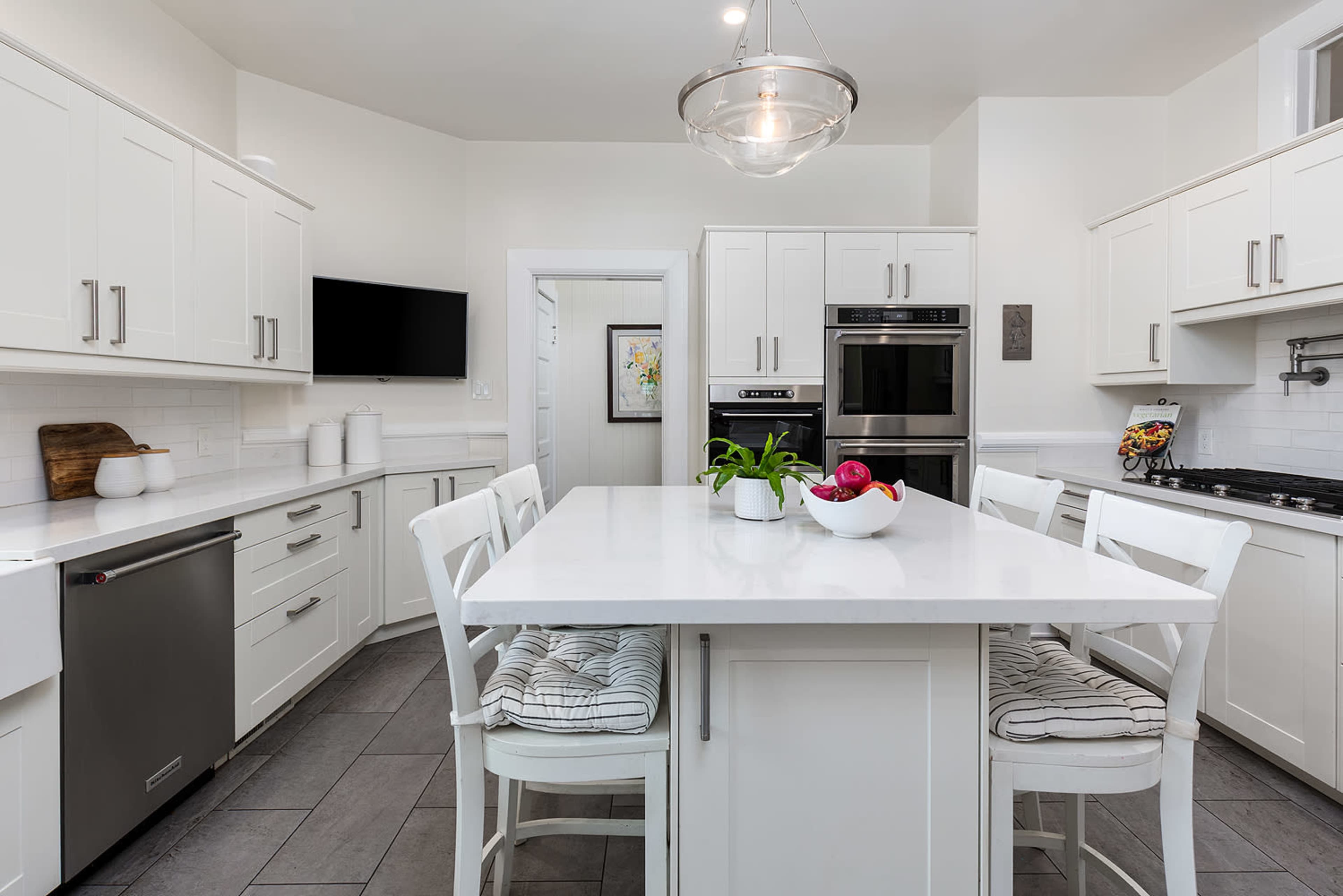 The image shows a modern kitchen with white cabinetry, a central island with bar stools, and stainless steel appliances.