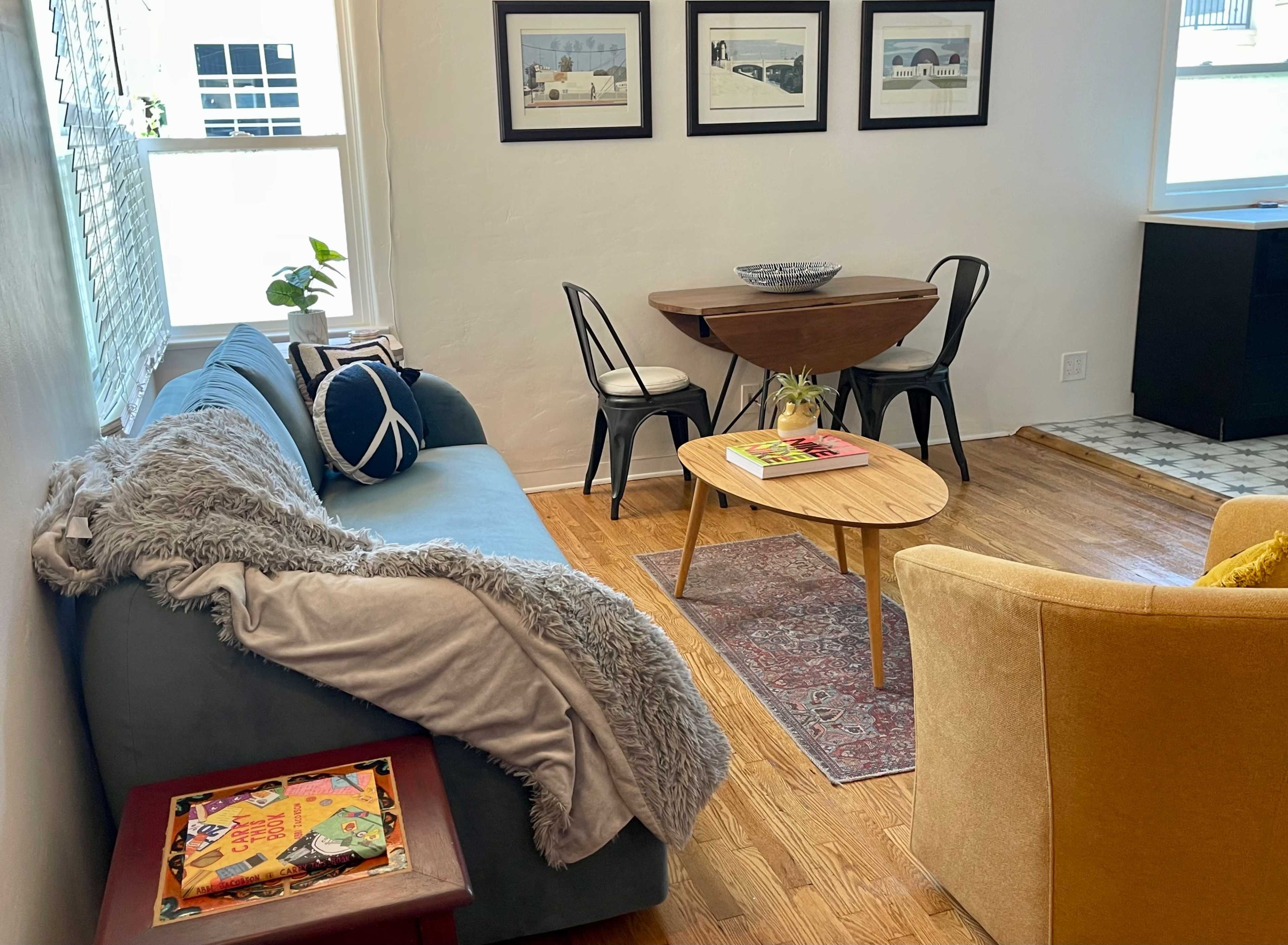 A cozy living room with a blue sofa draped with a gray blanket, a wooden coffee table, and framed photographs on the walls.
