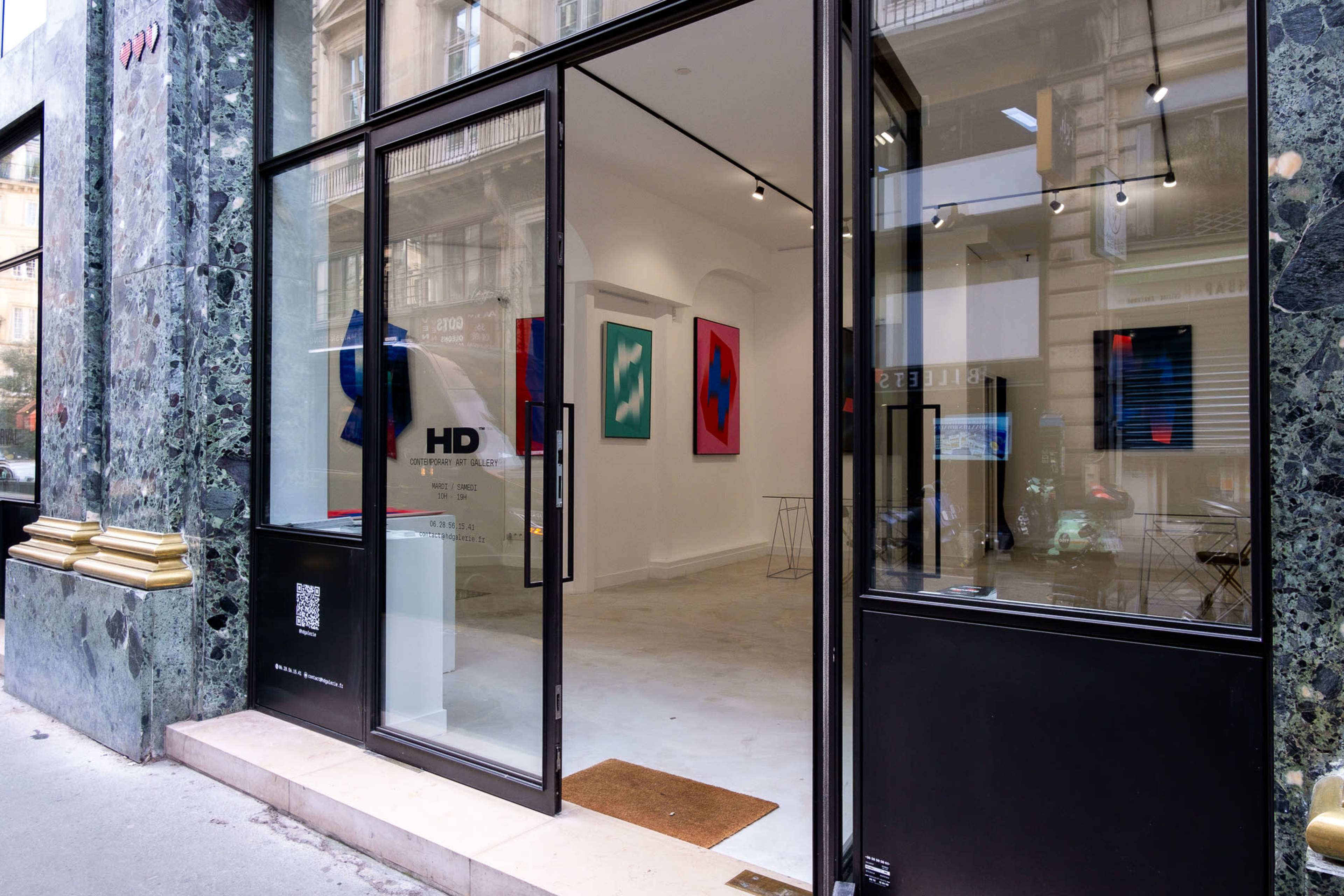 The entrance of an art gallery with modern artwork displayed through the large glass doors.