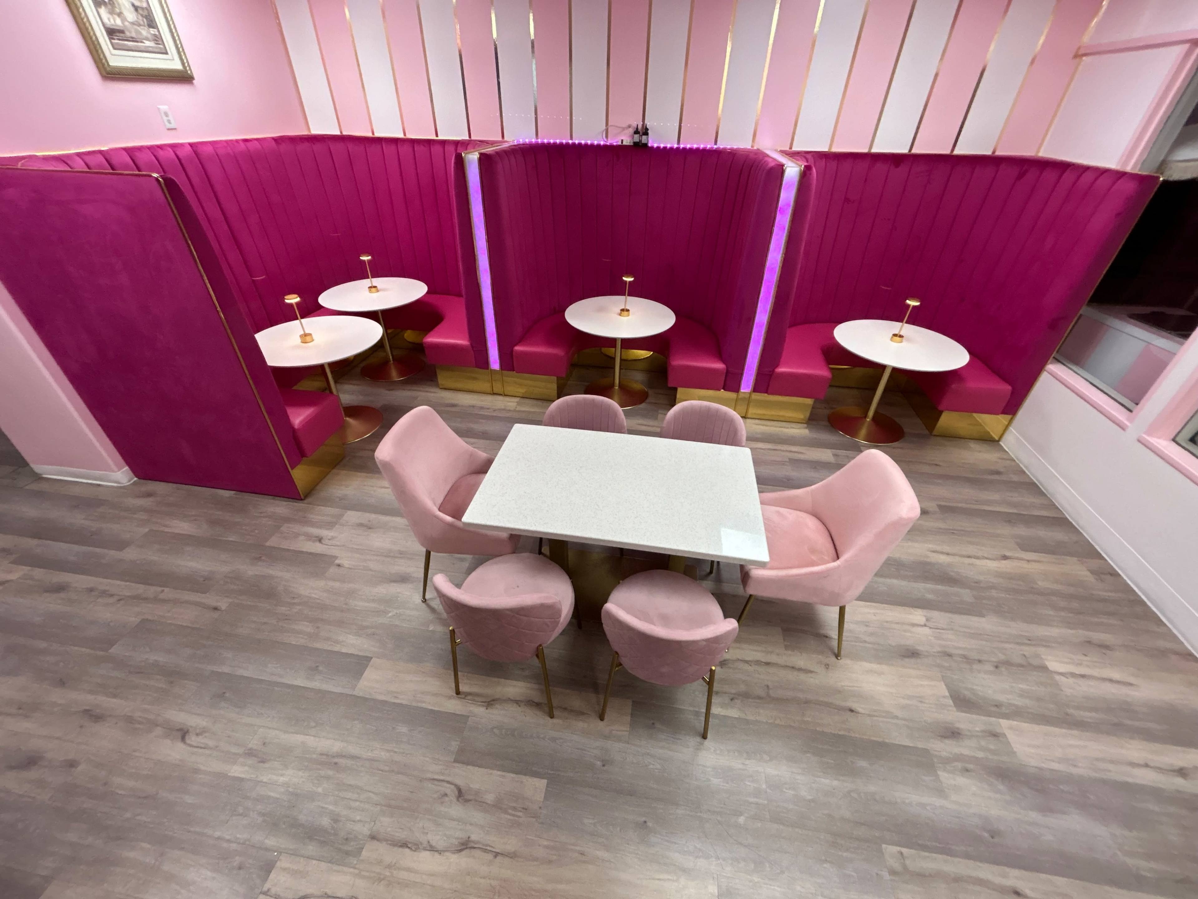 A café interior featuring pink walls and seating with a combination of tables and plush chairs arranged in a cozy layout.
