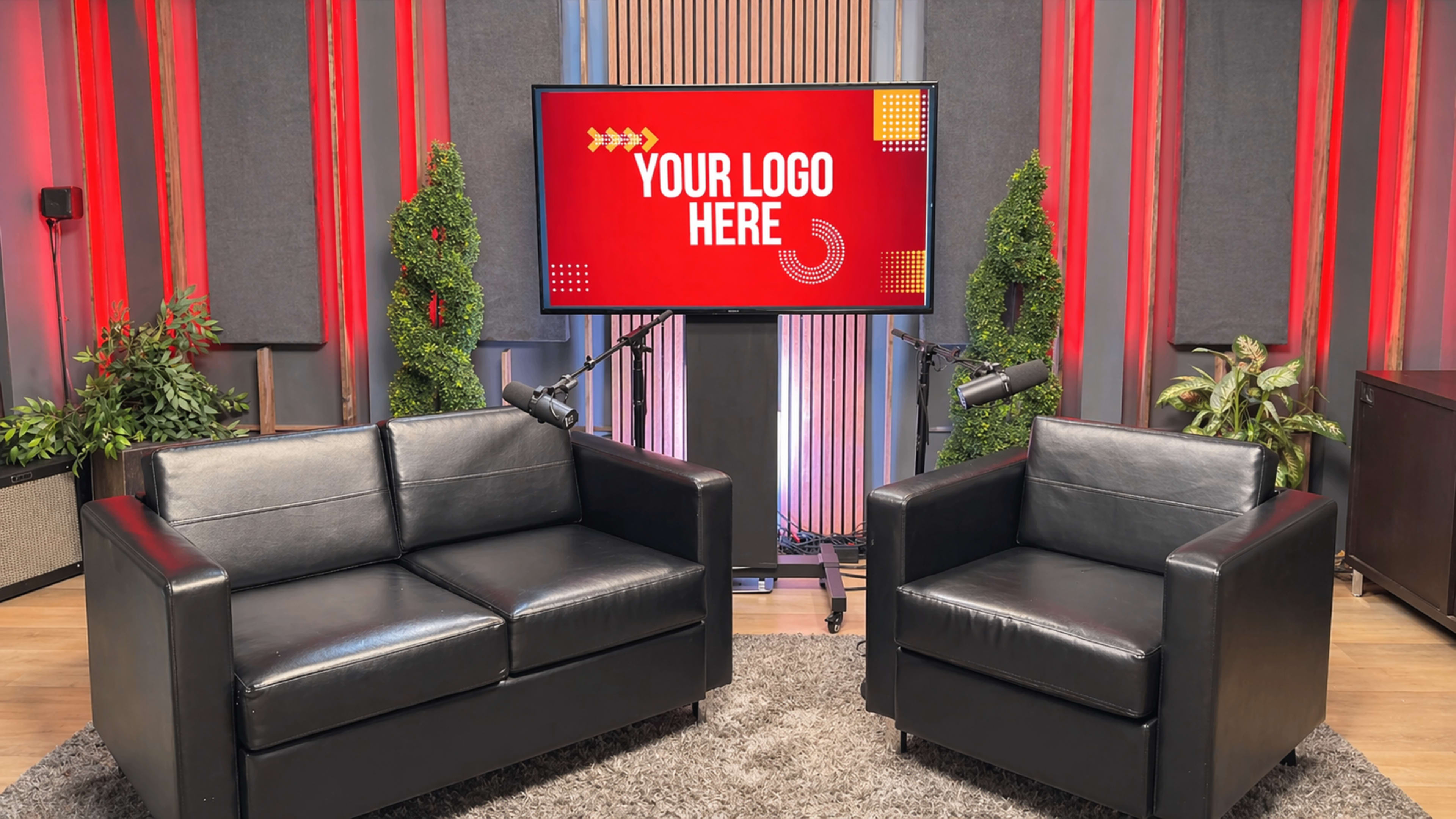 A modern studio setup features a black leather couch and armchair, with a large screen in the background displaying "YOUR LOGO HERE."