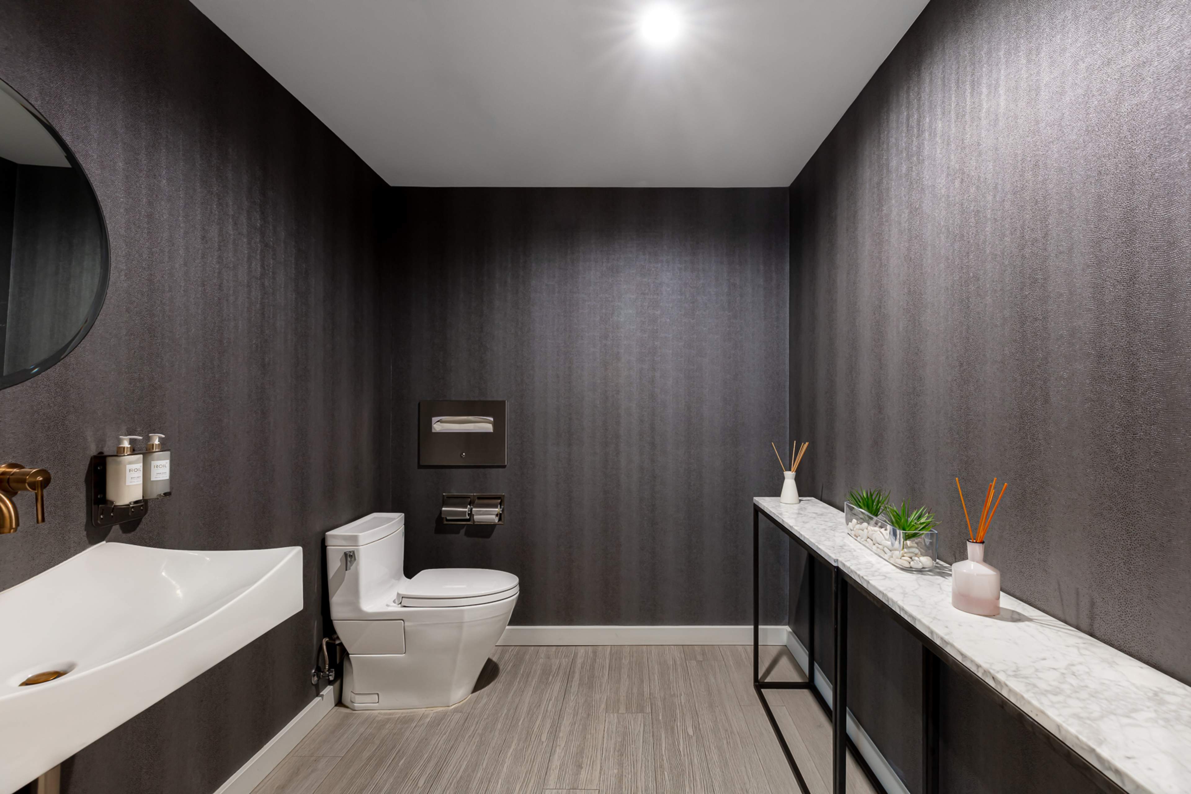 A modern bathroom featuring a toilet, a wall-mounted sink, a mirror, and a console table adorned with decorative elements.