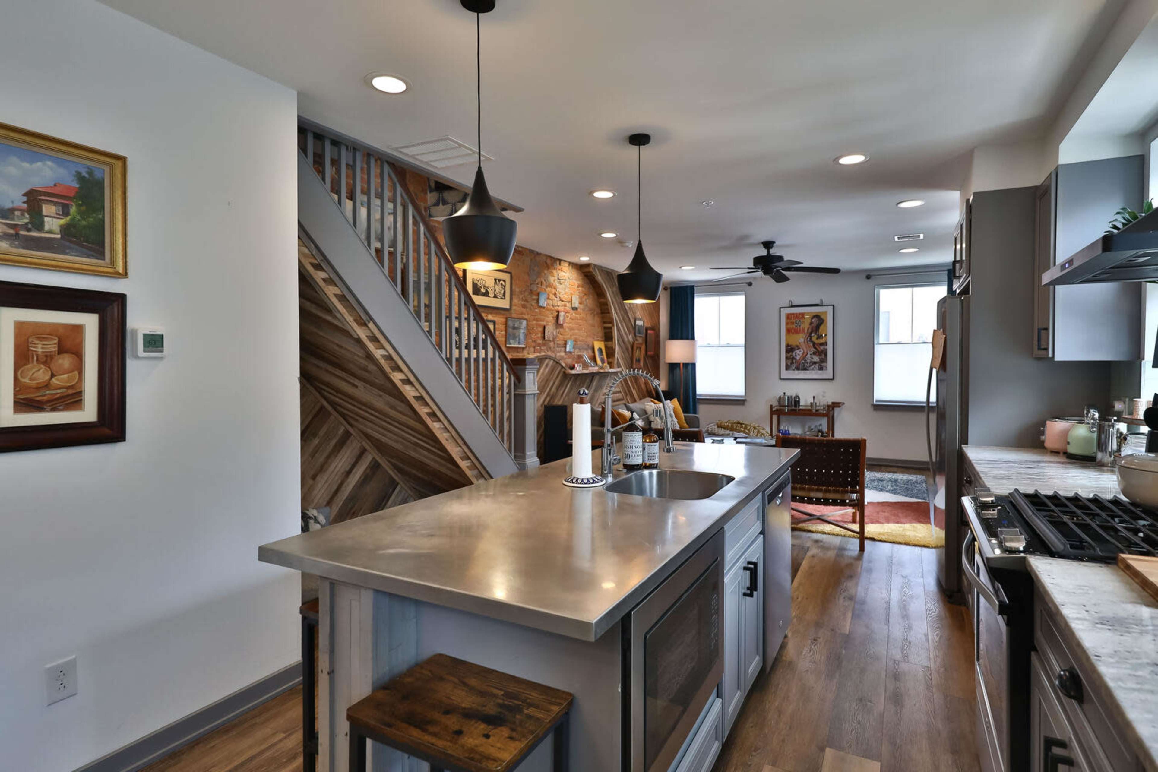 A modern kitchen with a concrete island, exposed brick wall, and wooden staircase leading to an upper level.