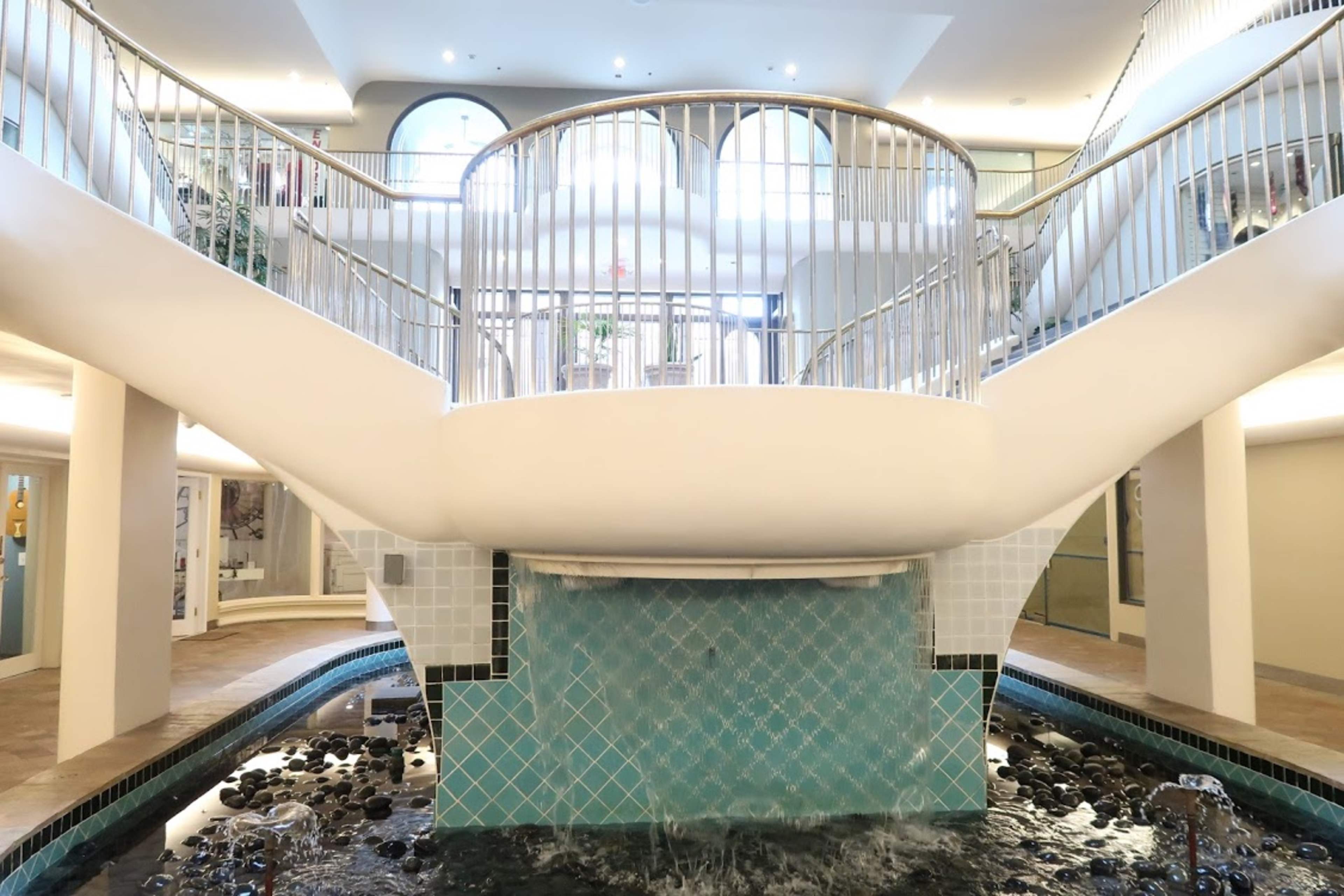 A modern interior featuring a central staircase with curved railings surrounded by a shallow water feature and tiled walls.